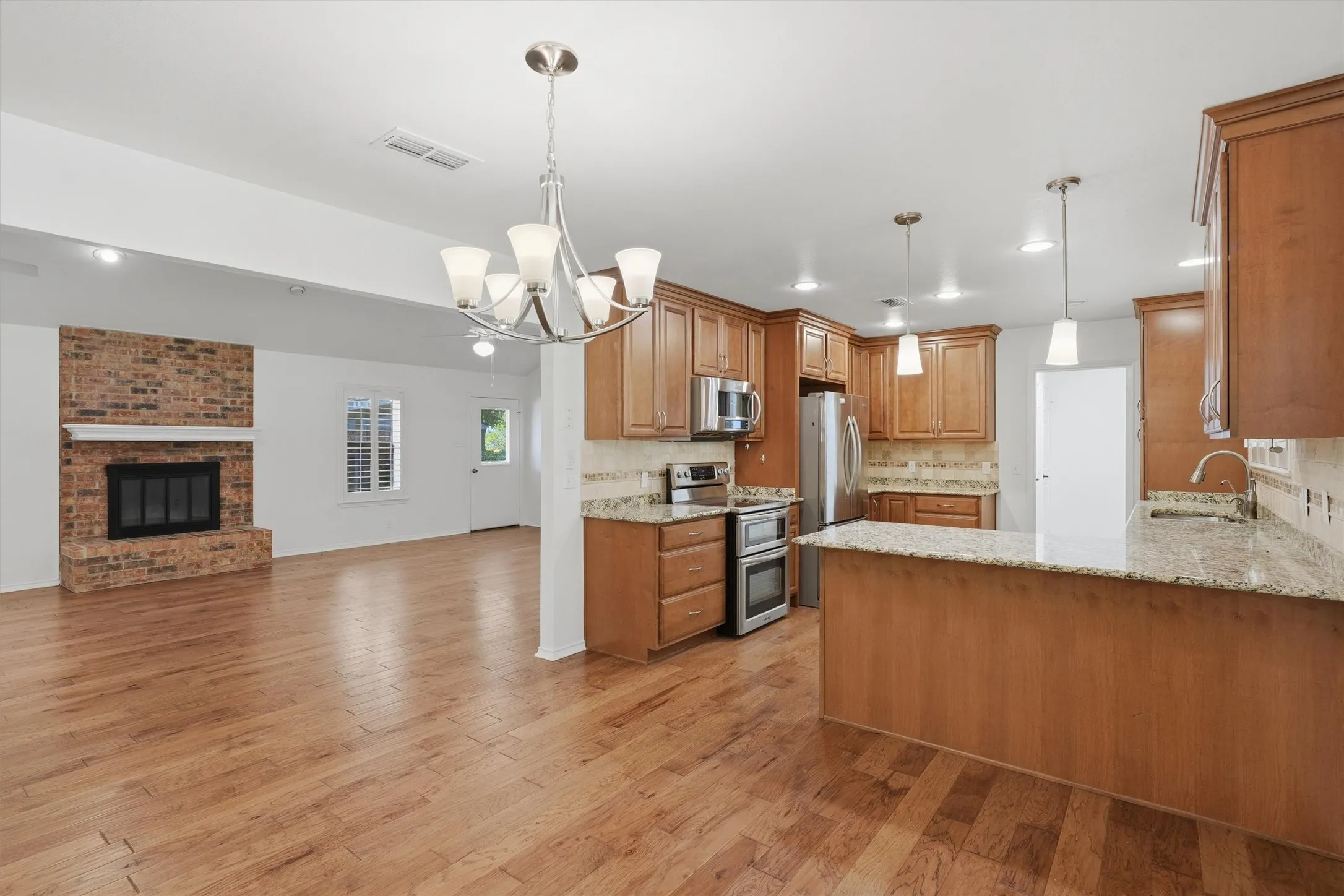 Wood-finish flooring throughout, kitchen with wood cabinetry and granite countertops, stainless steel appliances, and a brick fireplace