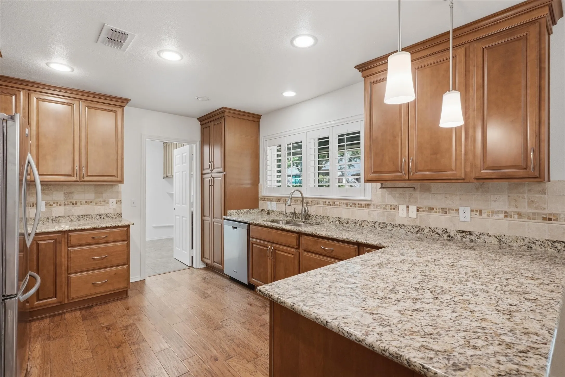 Kitchen featuring wood-finish flooring, recessed lighting, wood cabinetry, stone countertops, and a tile backsplash