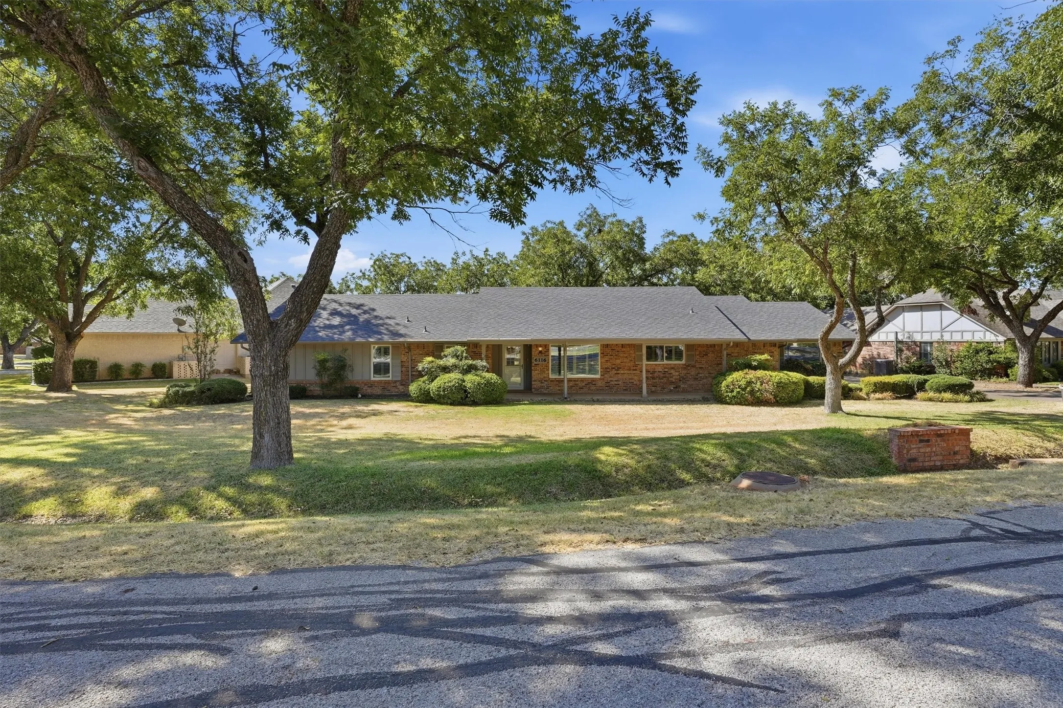 Brick and siding exterior with a dark shingle roof, established landscaping, and mature trees