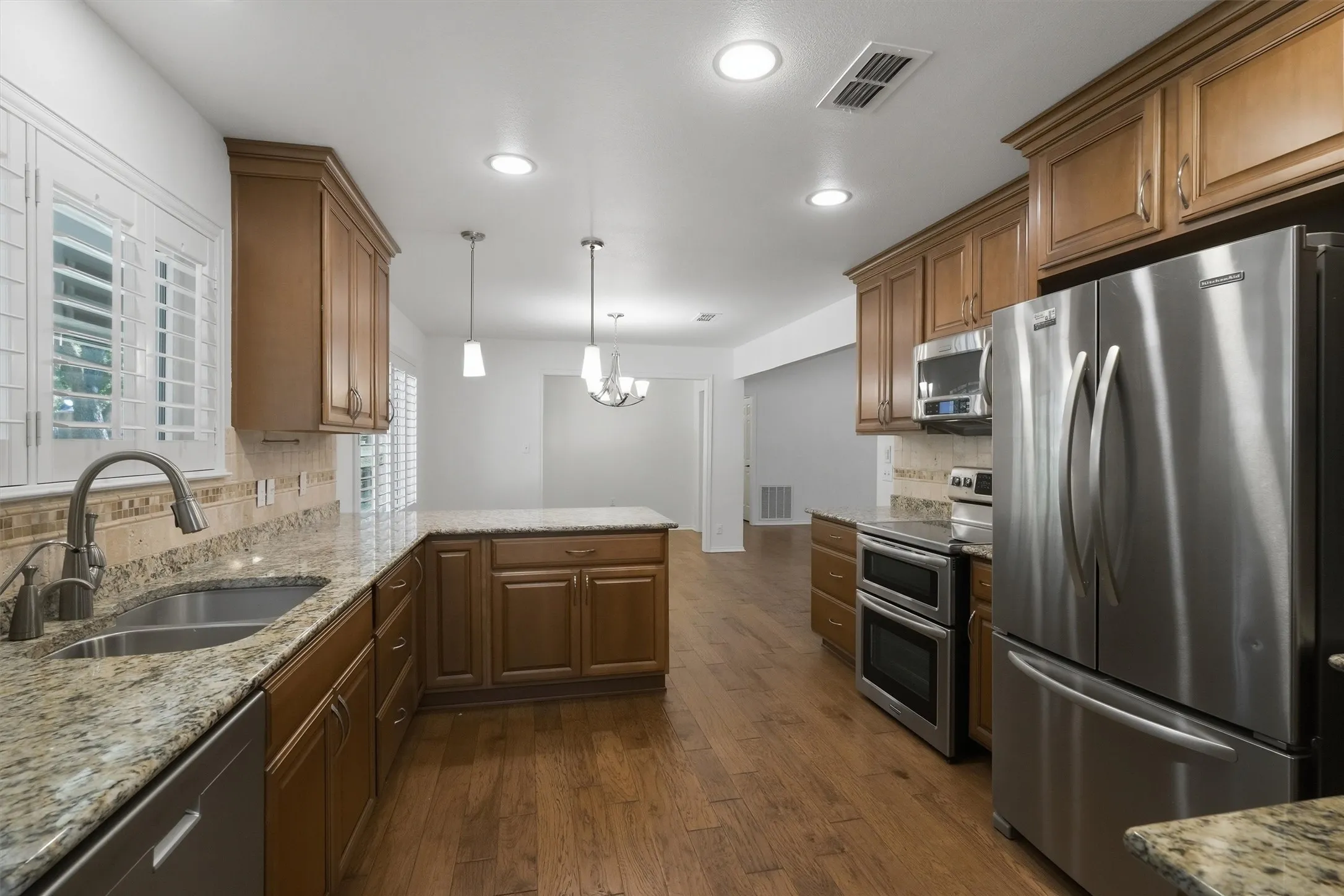 Kitchen featuring wood-finish flooring, wood cabinetry, granite countertops, stainless steel appliances, and recessed lighting