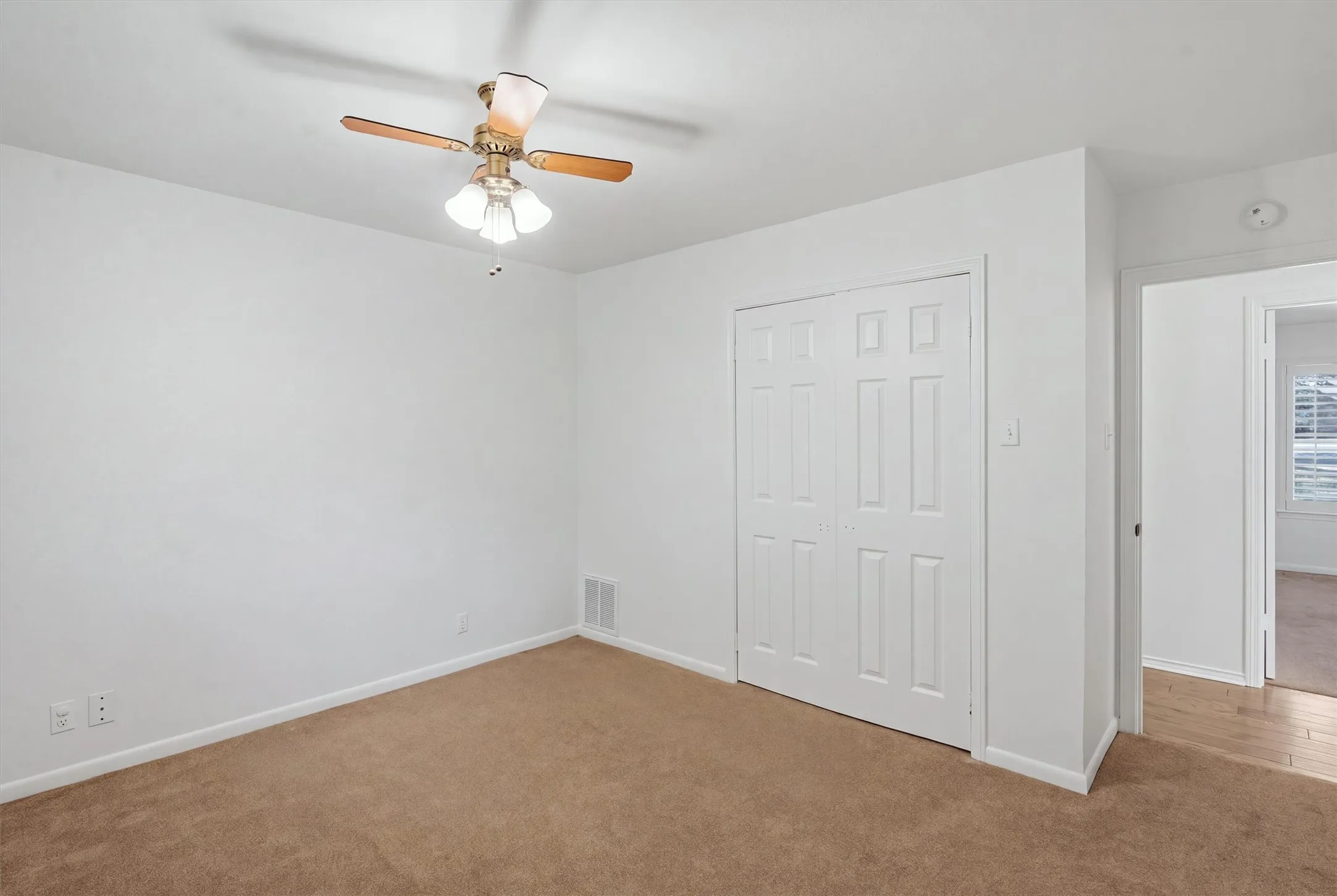 Carpeted room with a ceiling fan, white bi-fold closet doors, and light-colored walls
