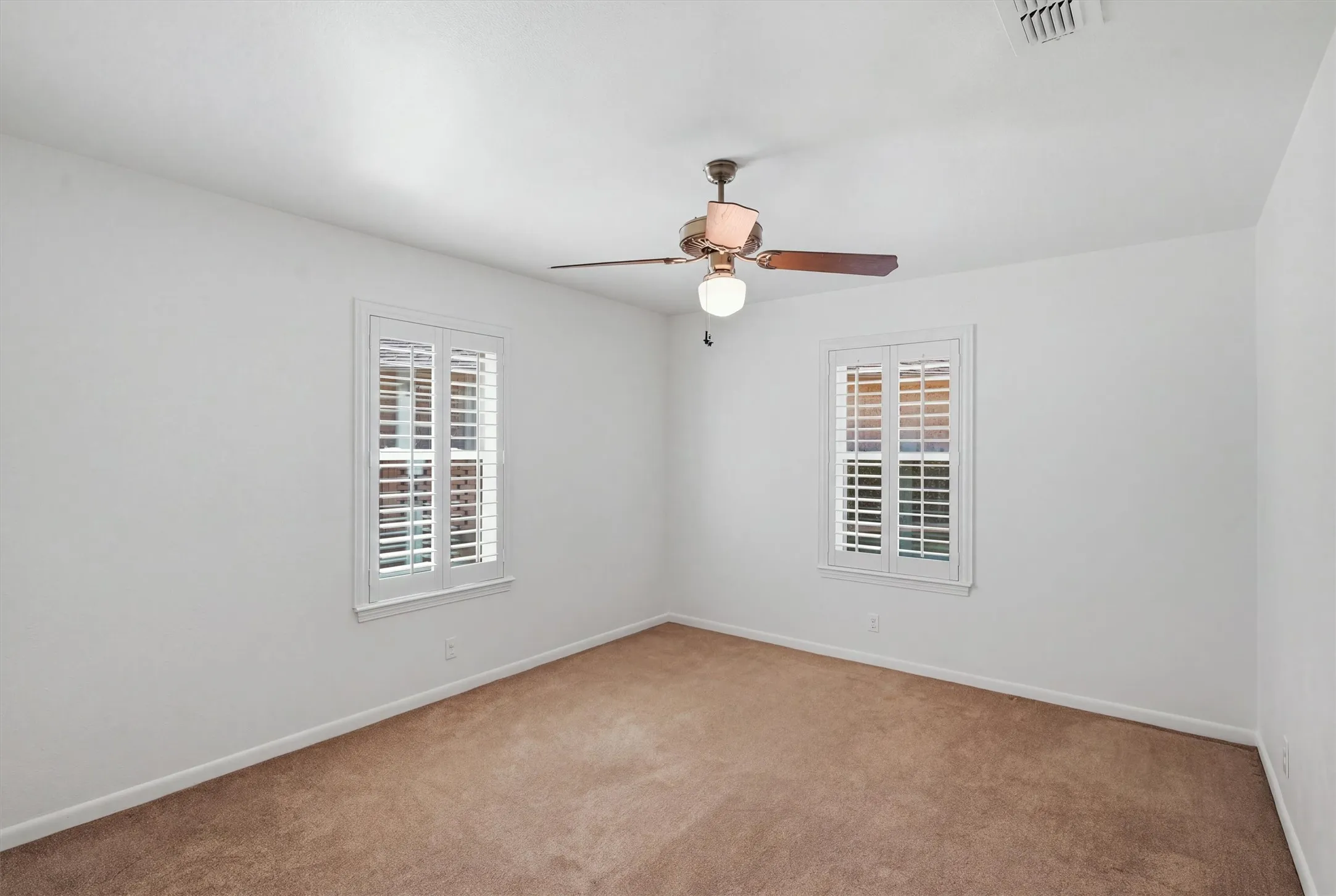 Two windows with plantation shutters, ceiling fan with integrated lighting, and neutral carpet