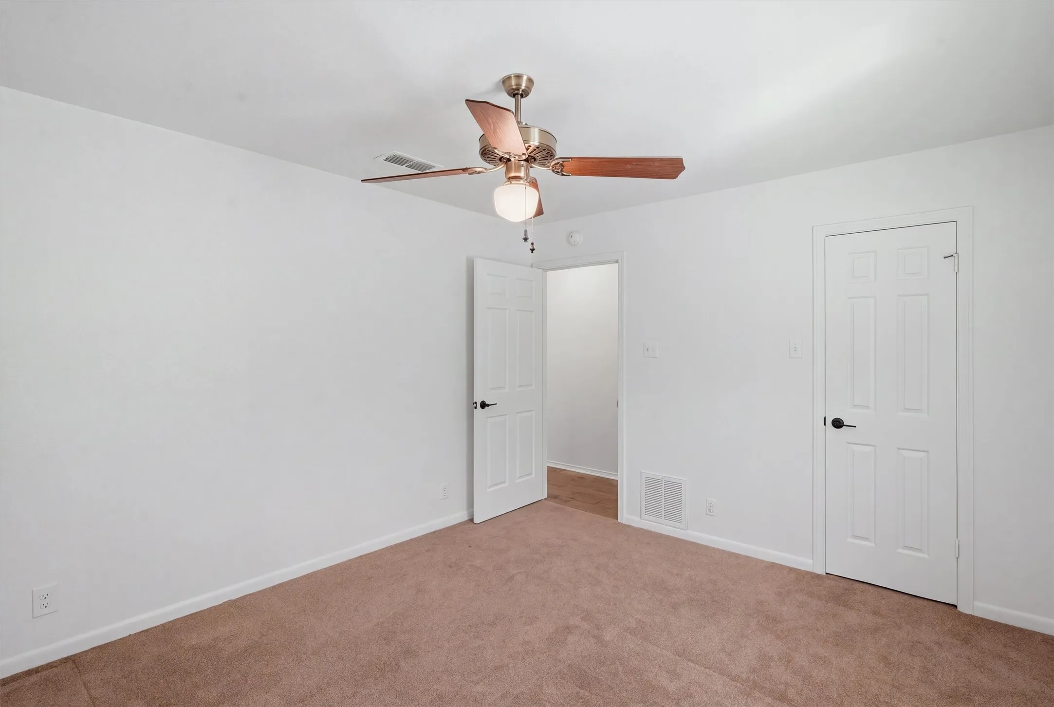 White walls, light brown carpeting, ceiling fan with integrated lighting, paneled interior doors, and black door hardware