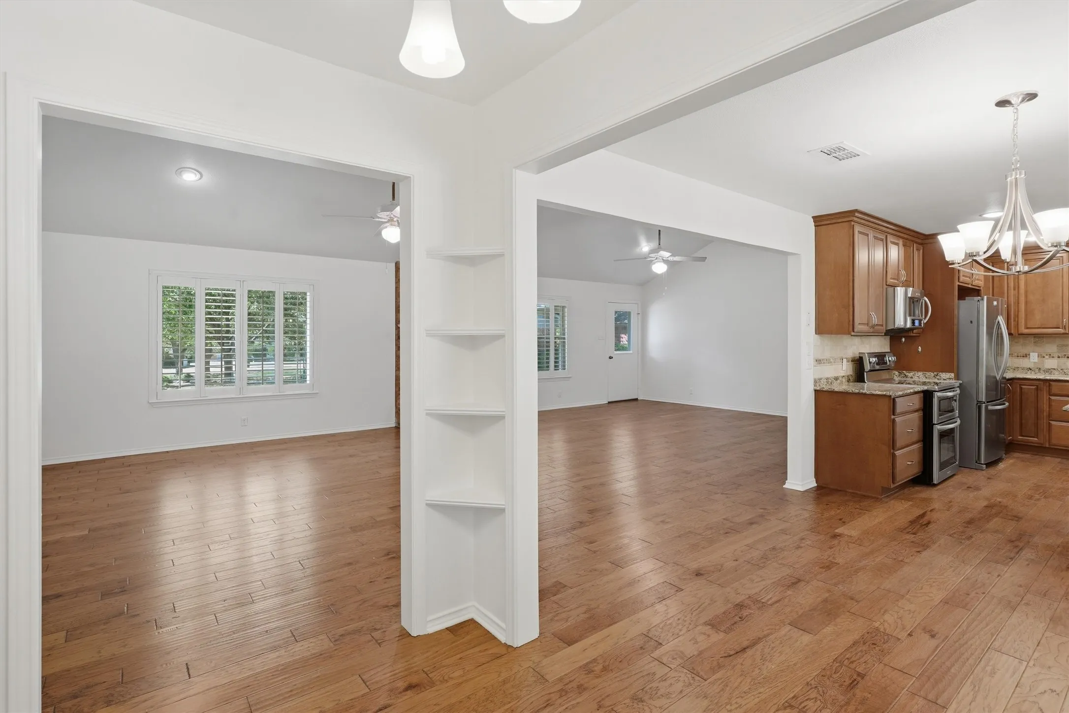 Expansive wood-finish flooring throughout, bright white walls, and a kitchen featuring wood cabinetry, stainless steel appliances, and a tile backsplash