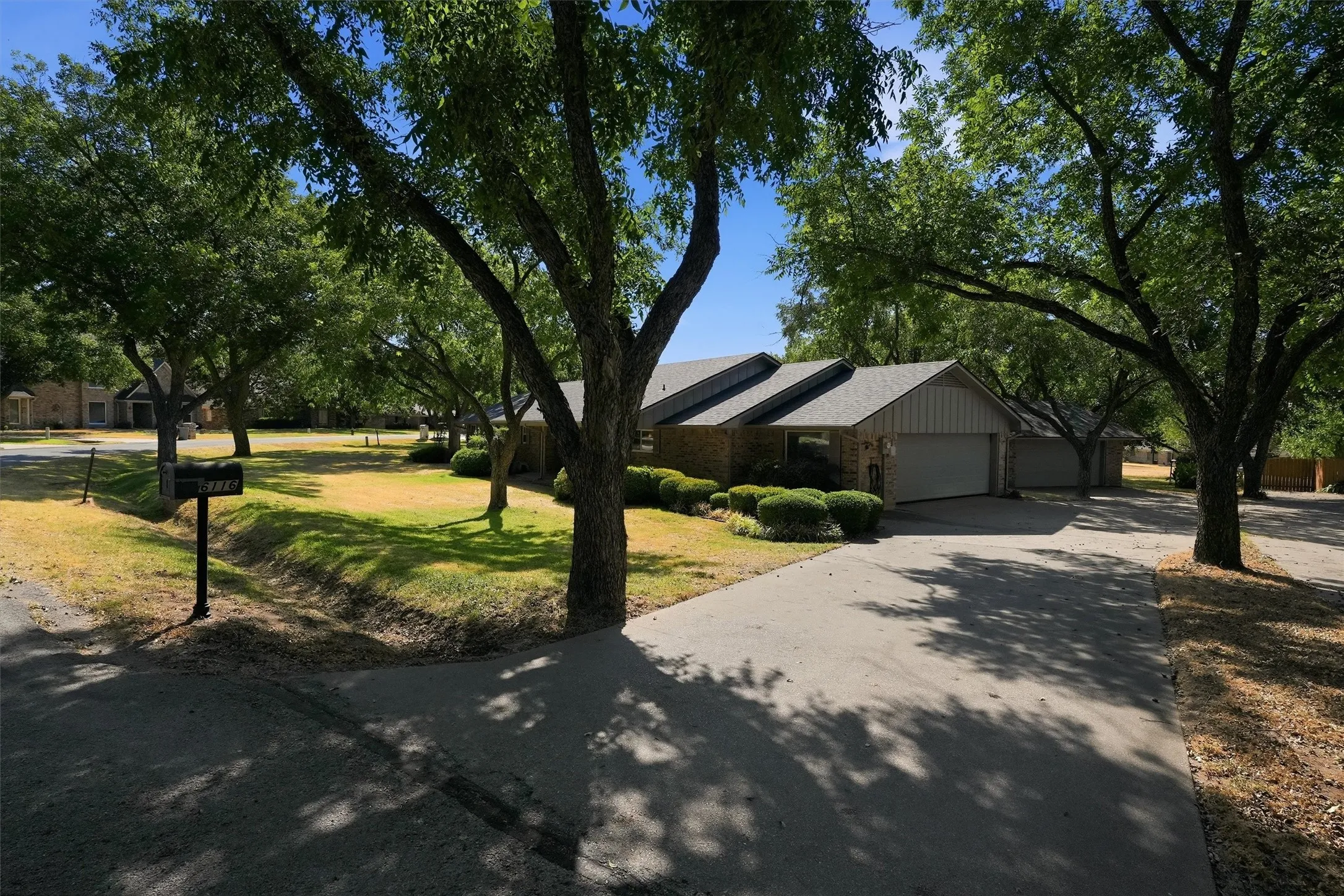 Brick exterior with a gray shingle roof, attached garage, paved driveway, and mature landscaping