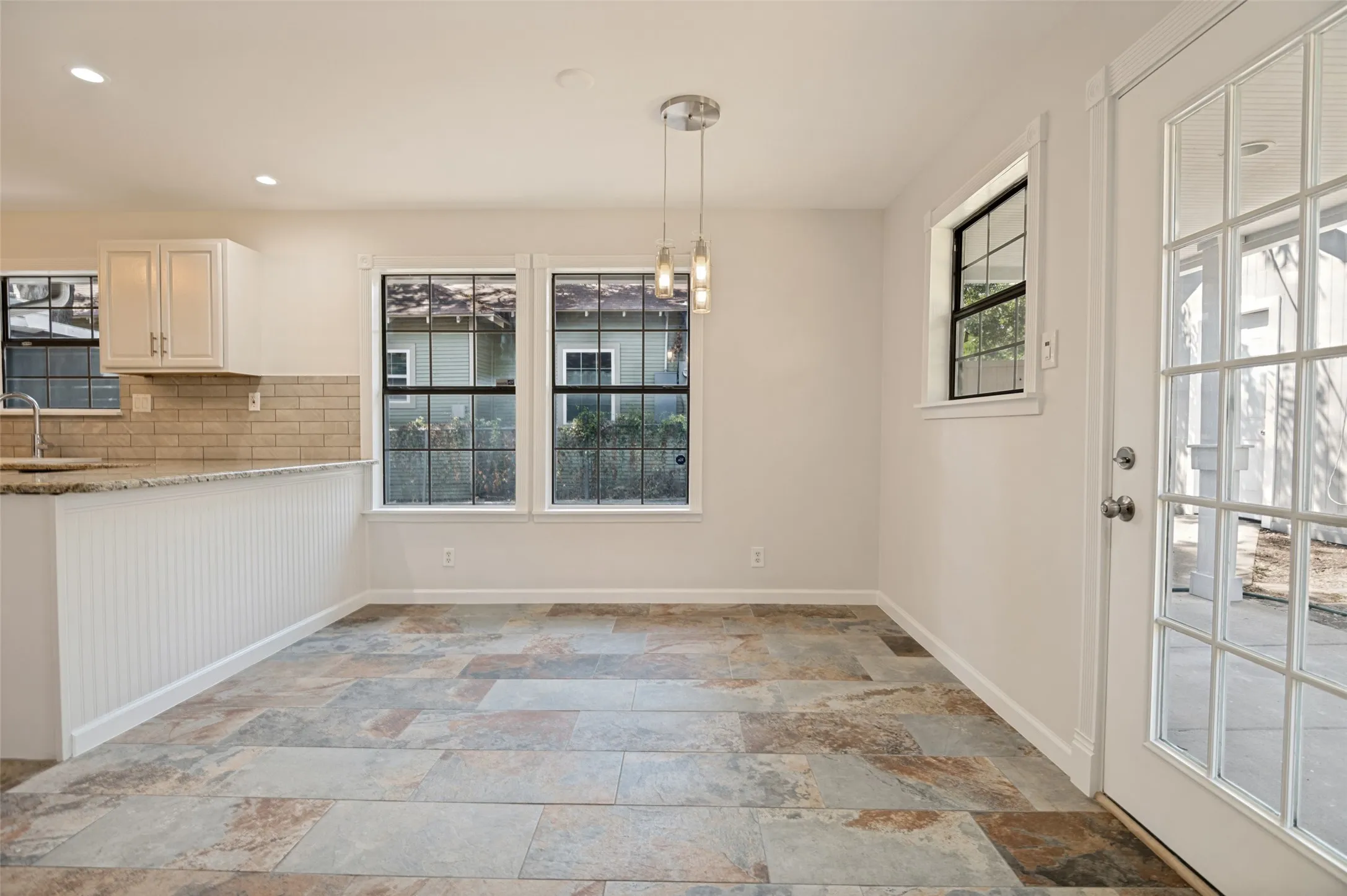 Expansive tile flooring, white shaker cabinetry, stainless steel sink, and a glass-paneled exterior door