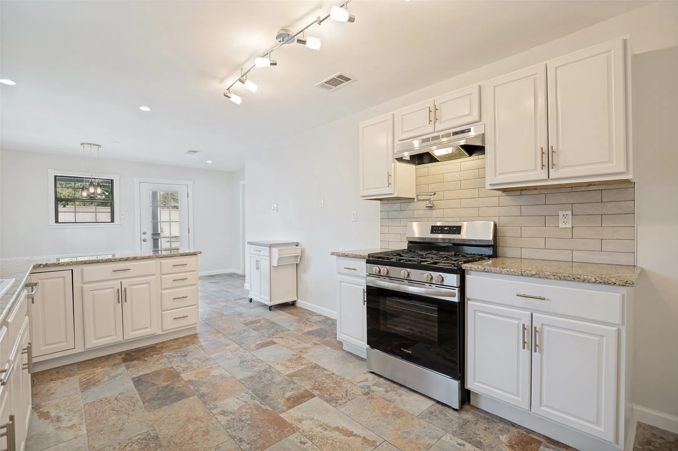Kitchen featuring white cabinetry, granite countertops, tile backsplash, stainless steel range with hood, and multi-tone tile flooring