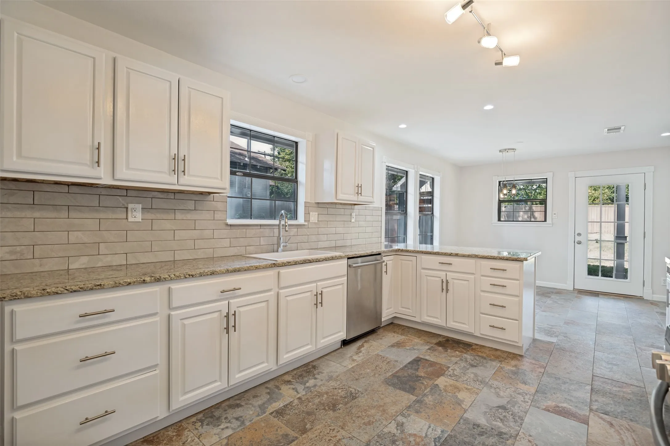 White cabinetry, light subway tile backsplash, granite countertops, stainless steel dishwasher, and slate-look tile flooring