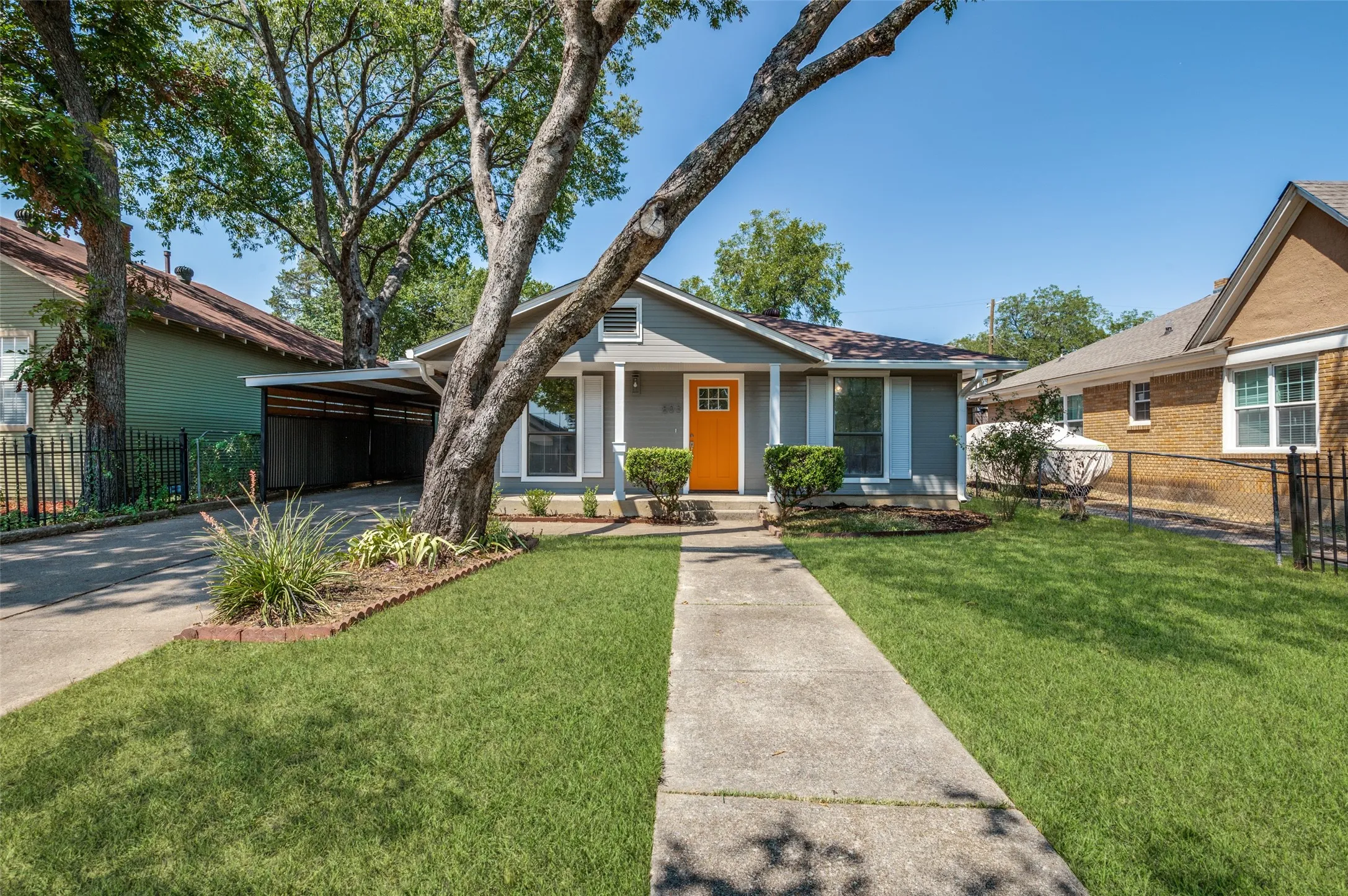 Single-story residence featuring a covered carport, a vibrant orange front door, a concrete walkway, and a manicured lawn