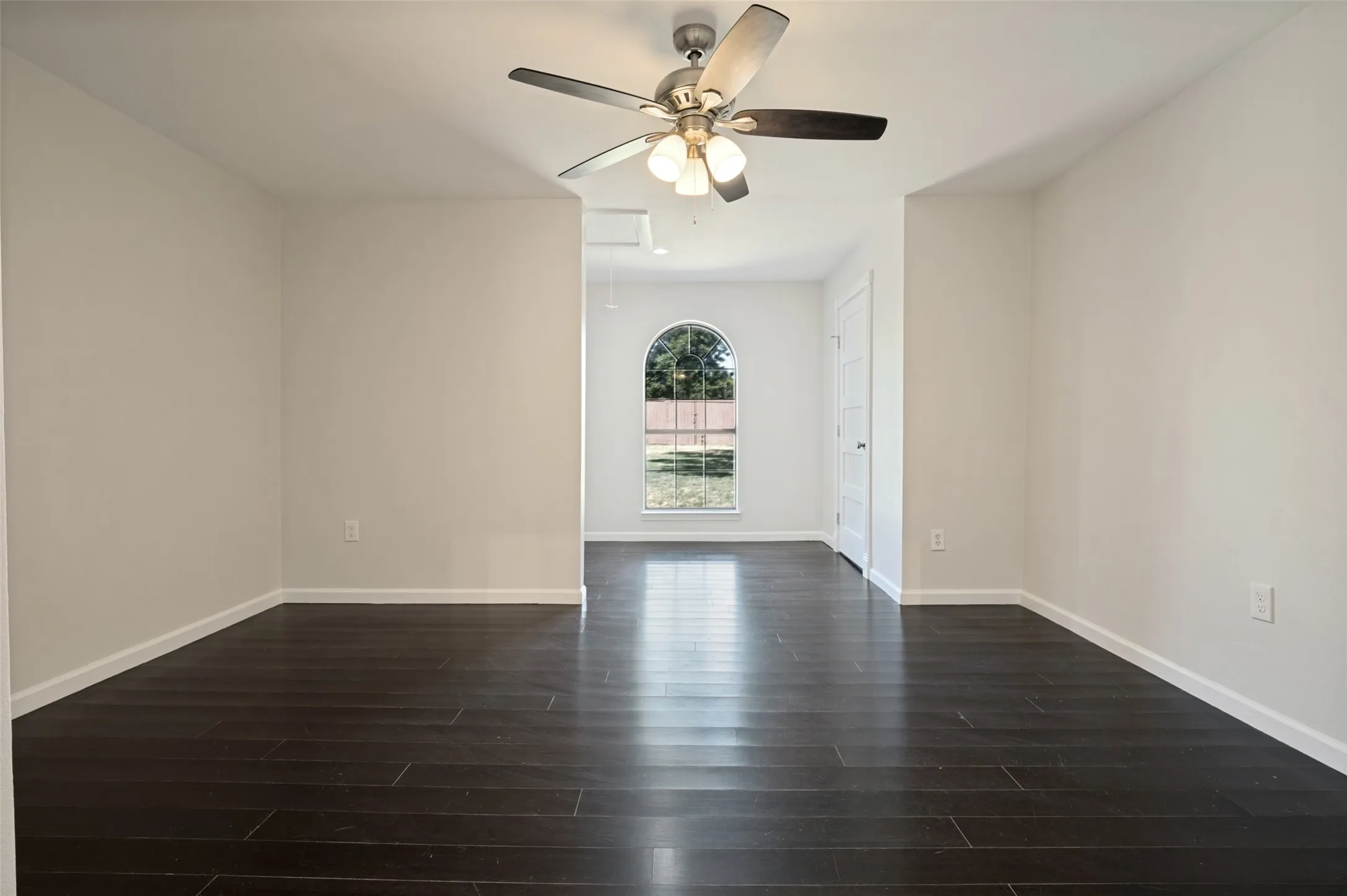 Hardwood-finish flooring, ceiling fan with integrated lighting, arched window, and white interior doors