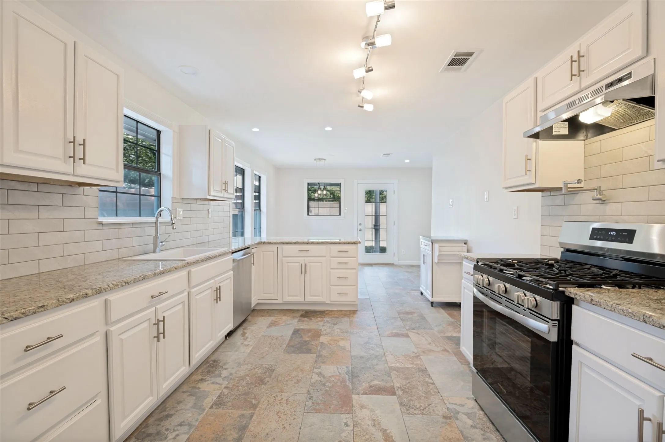 Spacious kitchen featuring white cabinetry, light-colored countertops, a tile backsplash, stainless steel appliances, and multi-toned tile flooring