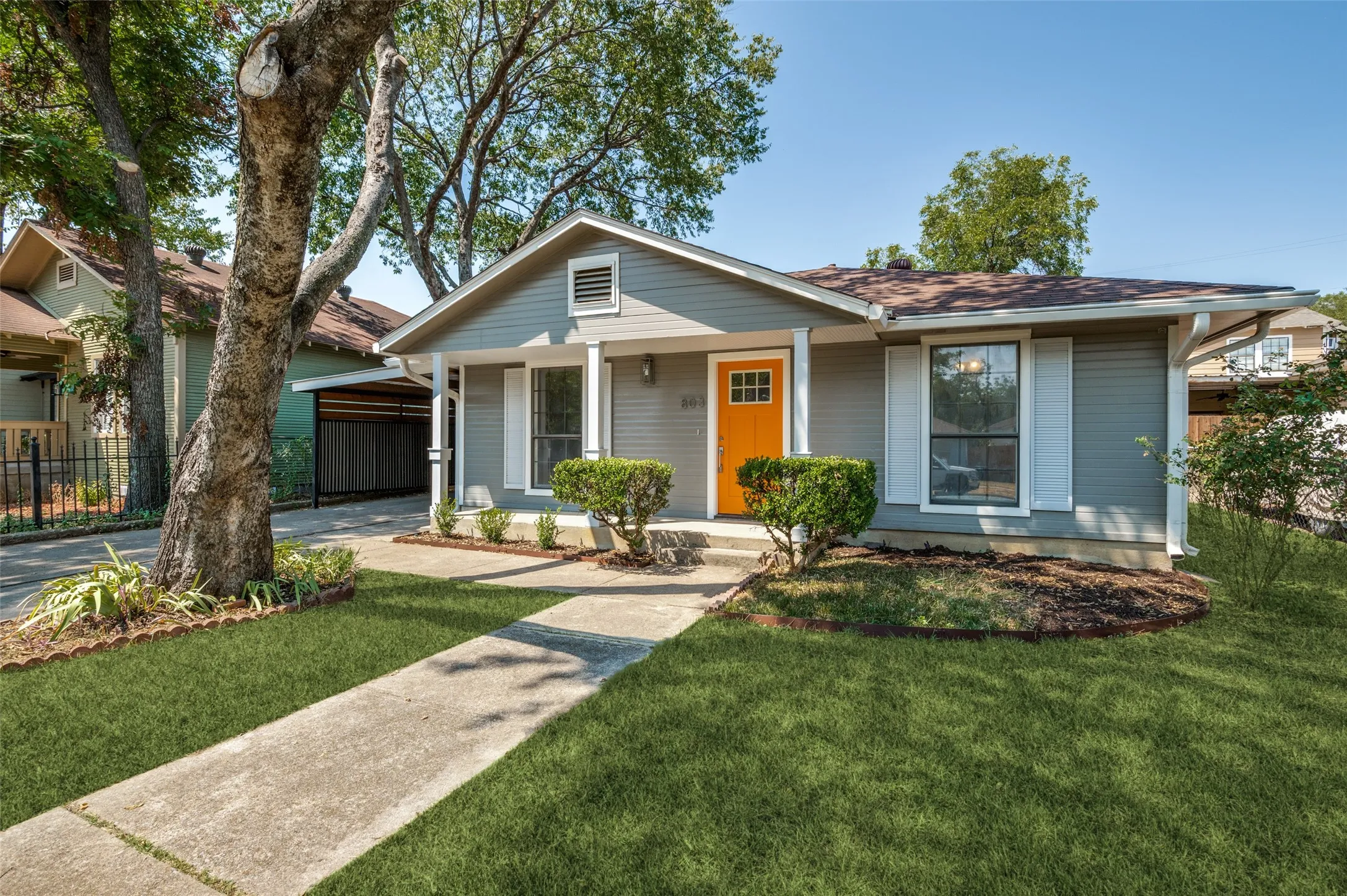 Gray siding exterior with white trim, a vibrant orange entry door, and a covered front porch