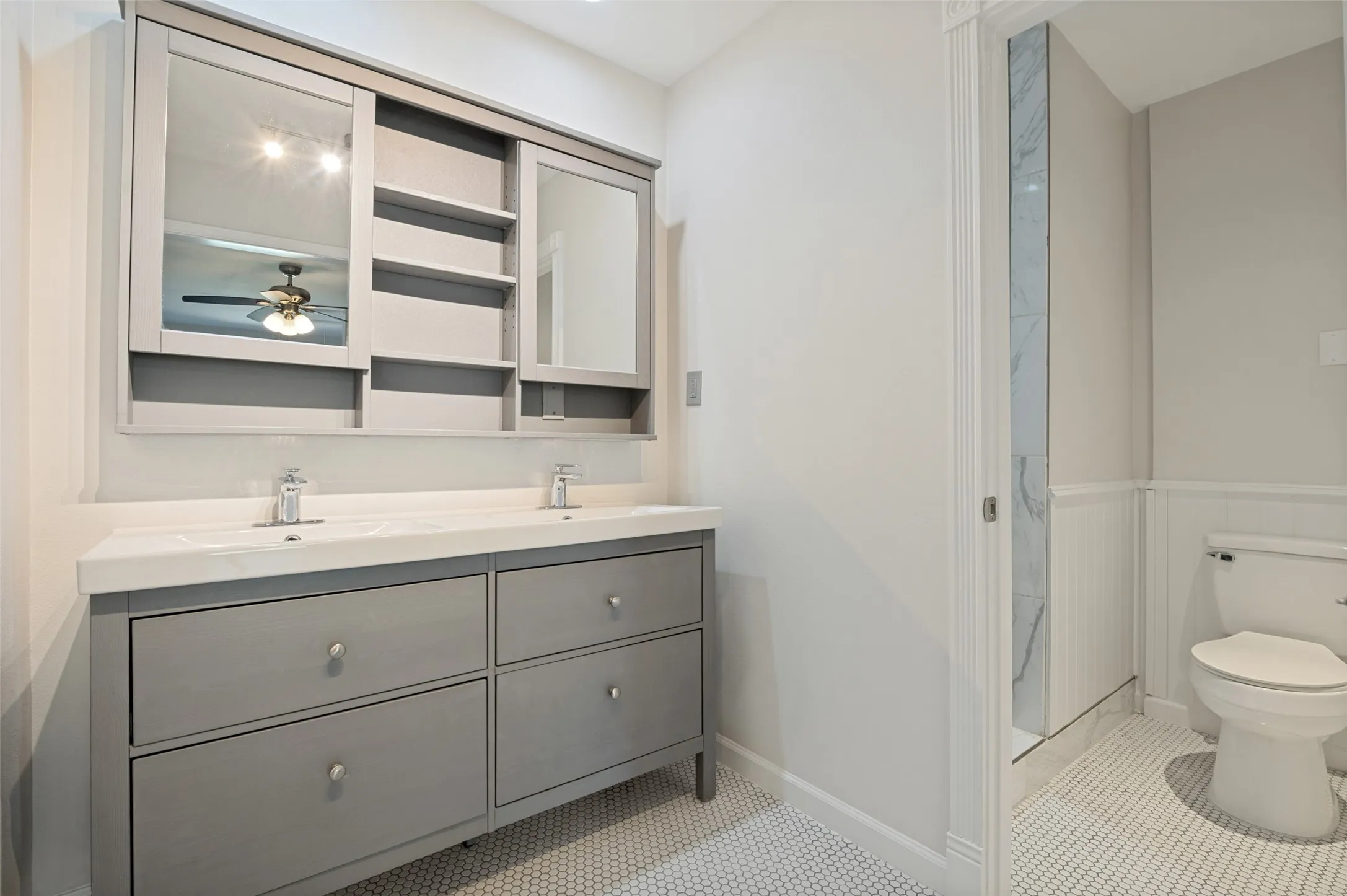 Dual vanity with integrated sinks, a built-in medicine cabinet with mirrored doors and open shelving, hexagon tile flooring, and wainscoting