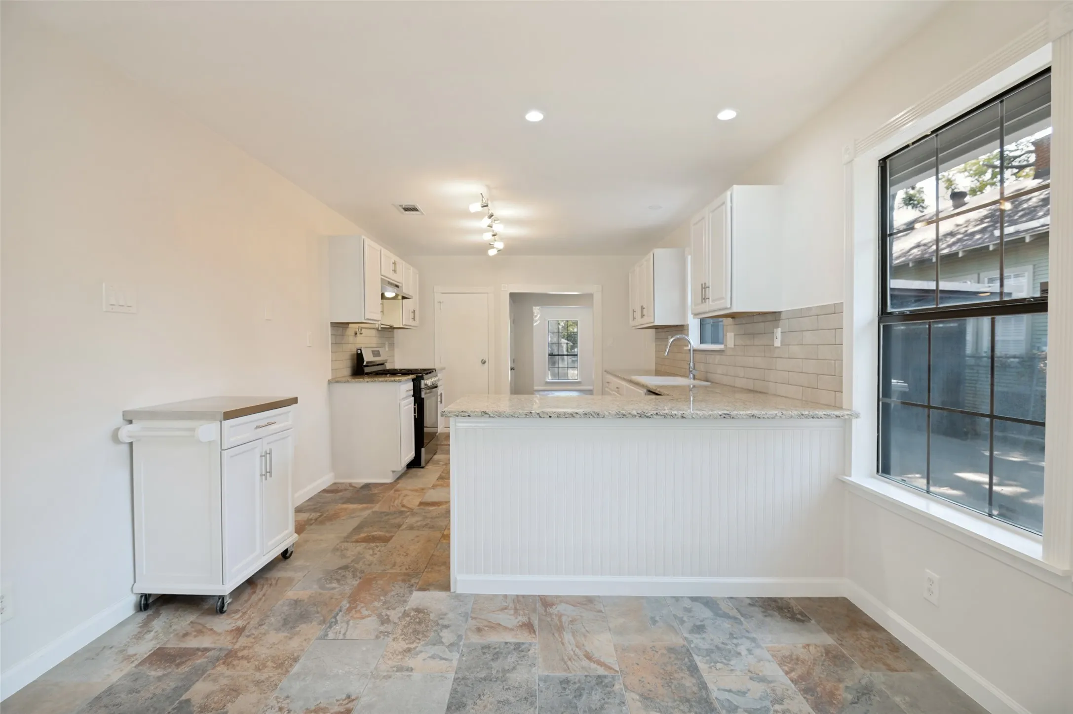 Kitchen featuring white cabinetry, subway tile backsplash, light-toned countertops, and multi-toned tile flooring