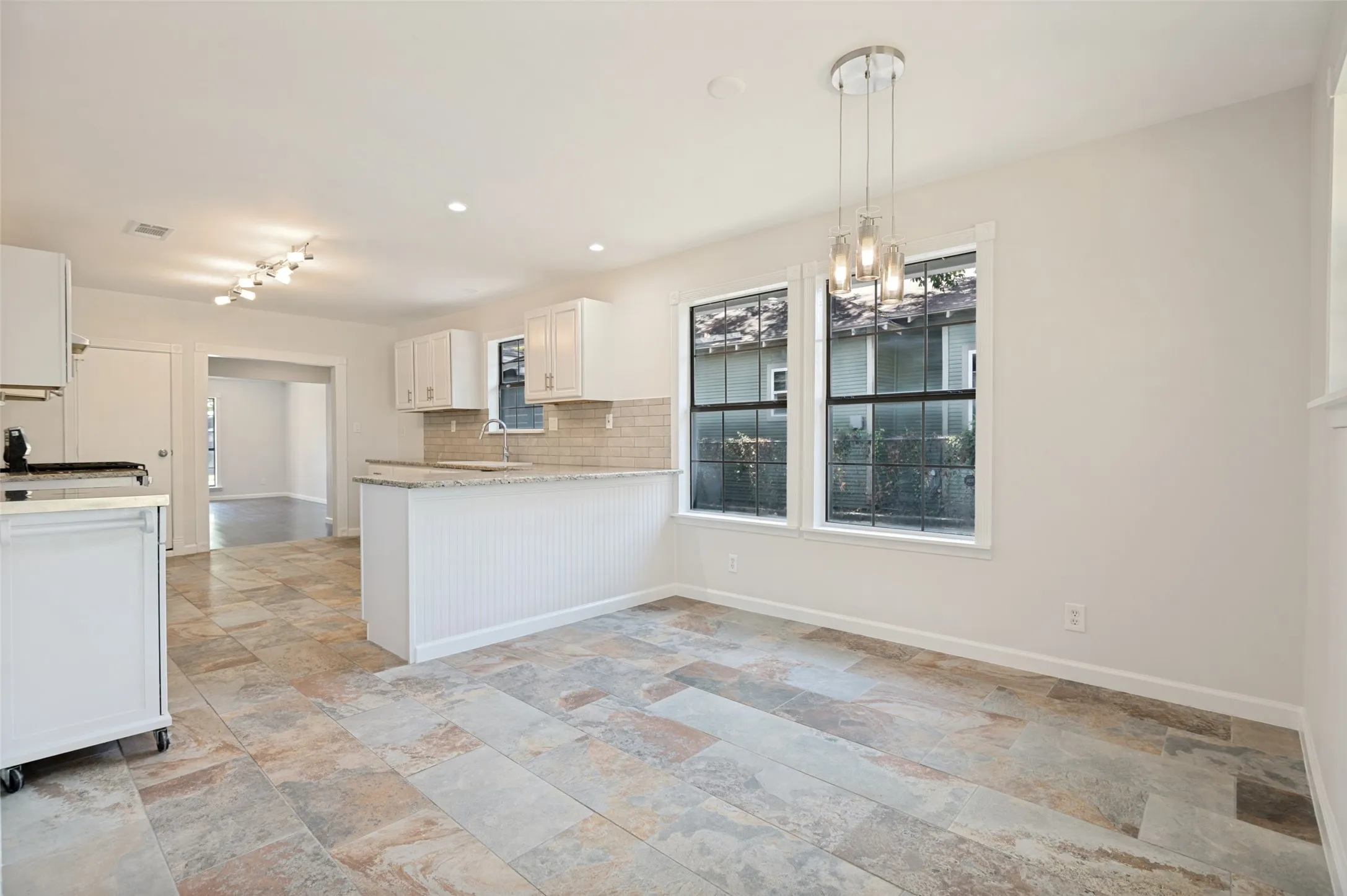 Spacious open-concept room featuring multi-toned tile flooring, white shaker cabinetry, a light-toned countertop, a tile backsplash, and a contemporary chandelier