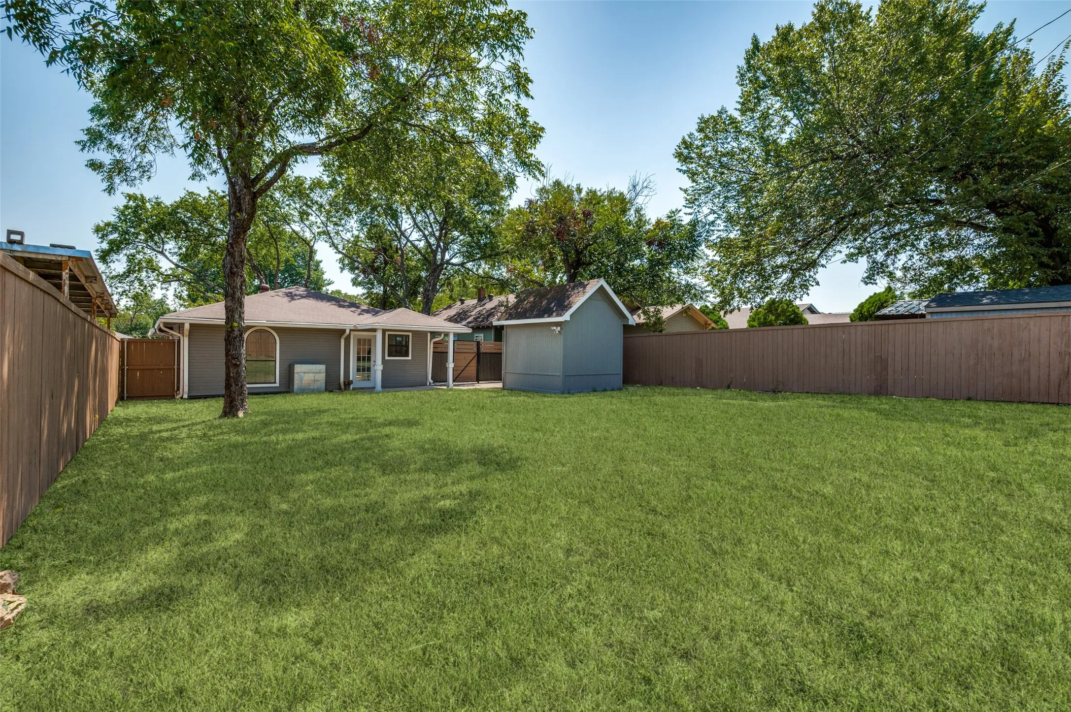 Expansive green space featuring a wood fence, mature trees, and a detached storage shed