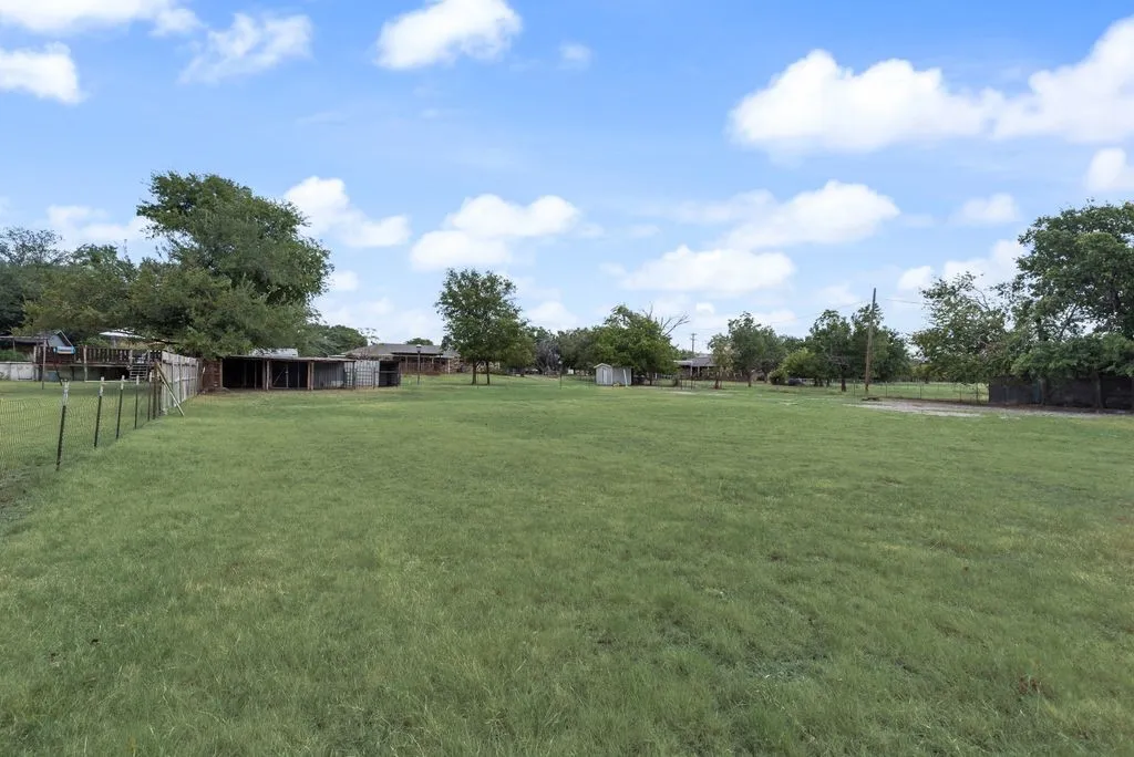 Expansive green lawn with a wire fence and mature trees