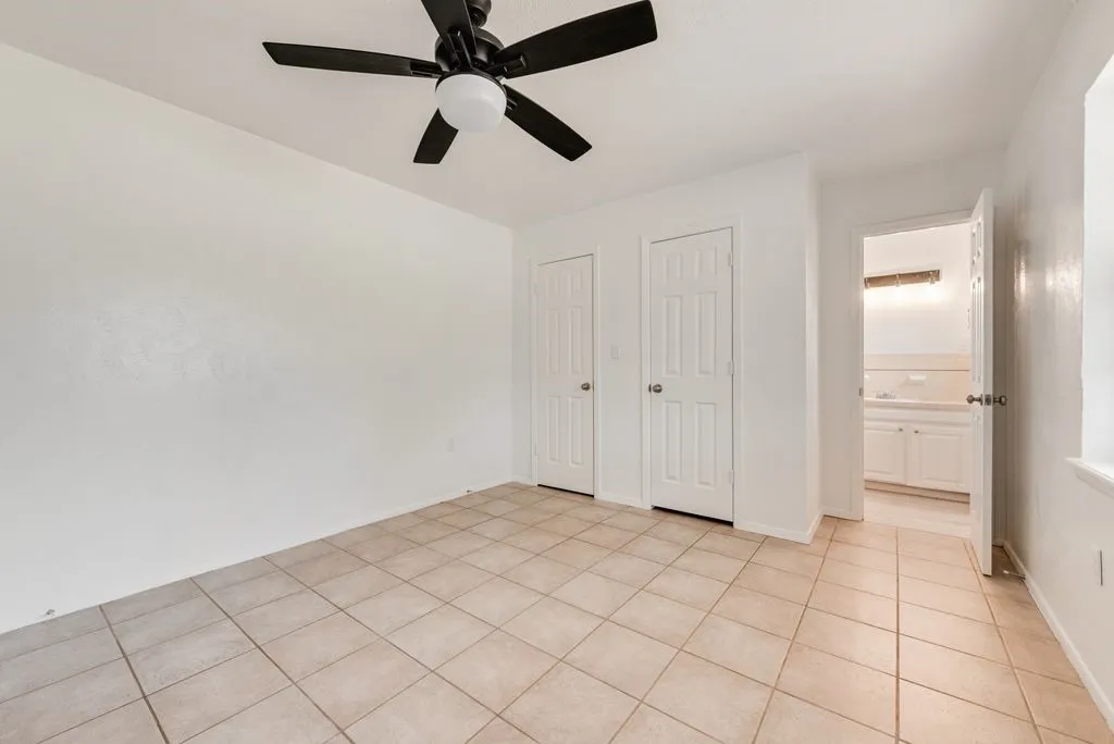 Neutral tone walls with a ceiling fan, tile flooring, and multiple closet doors