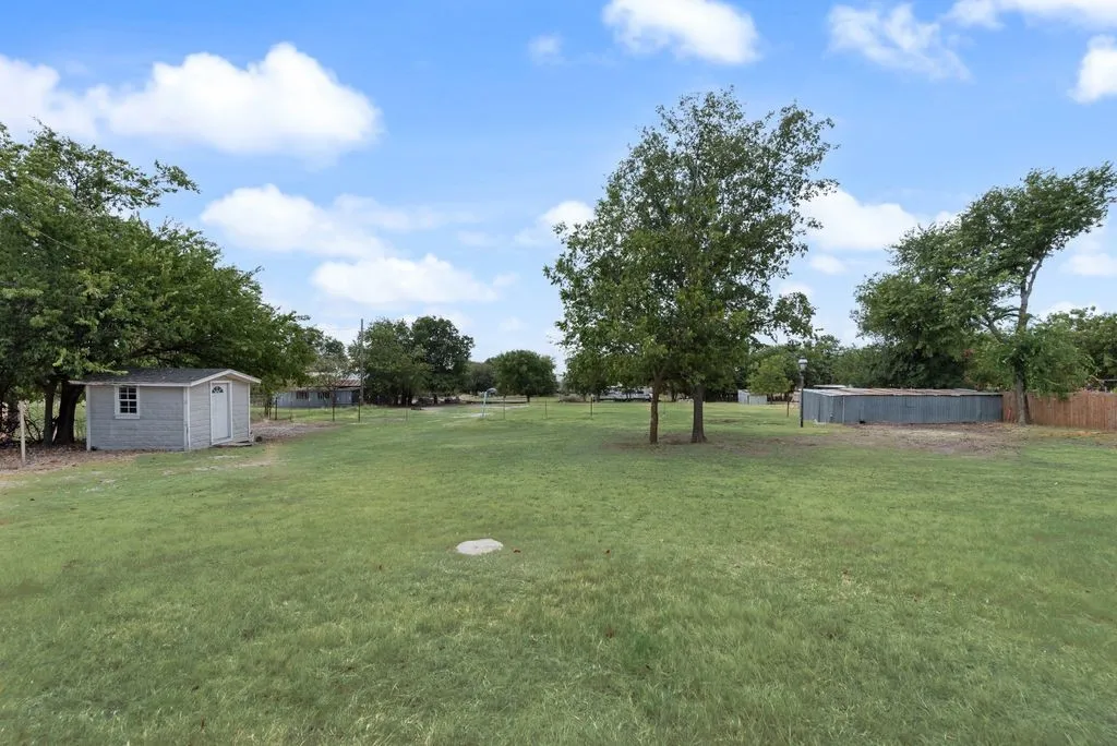 Expansive grass yard featuring mature trees, a small storage shed, and a privacy fence