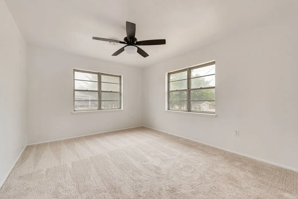 Spacious room with plush carpeting, neutral wall finishes, a modern ceiling fan, and two large windows