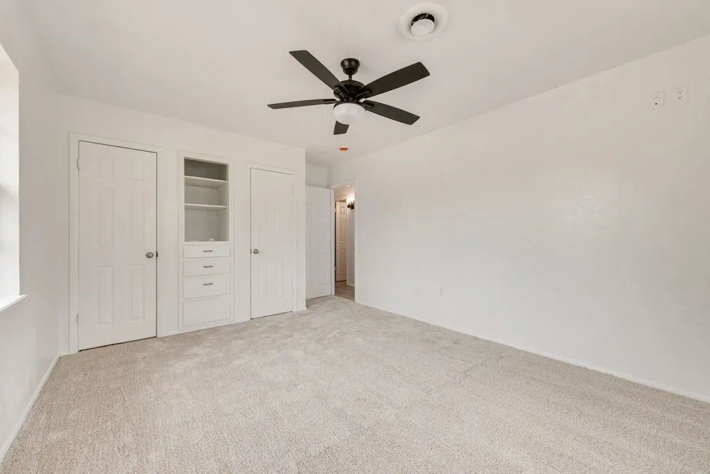 Spacious bedroom featuring neutral carpeting, ceiling fan with integrated lighting, and built-in cabinetry with shelving