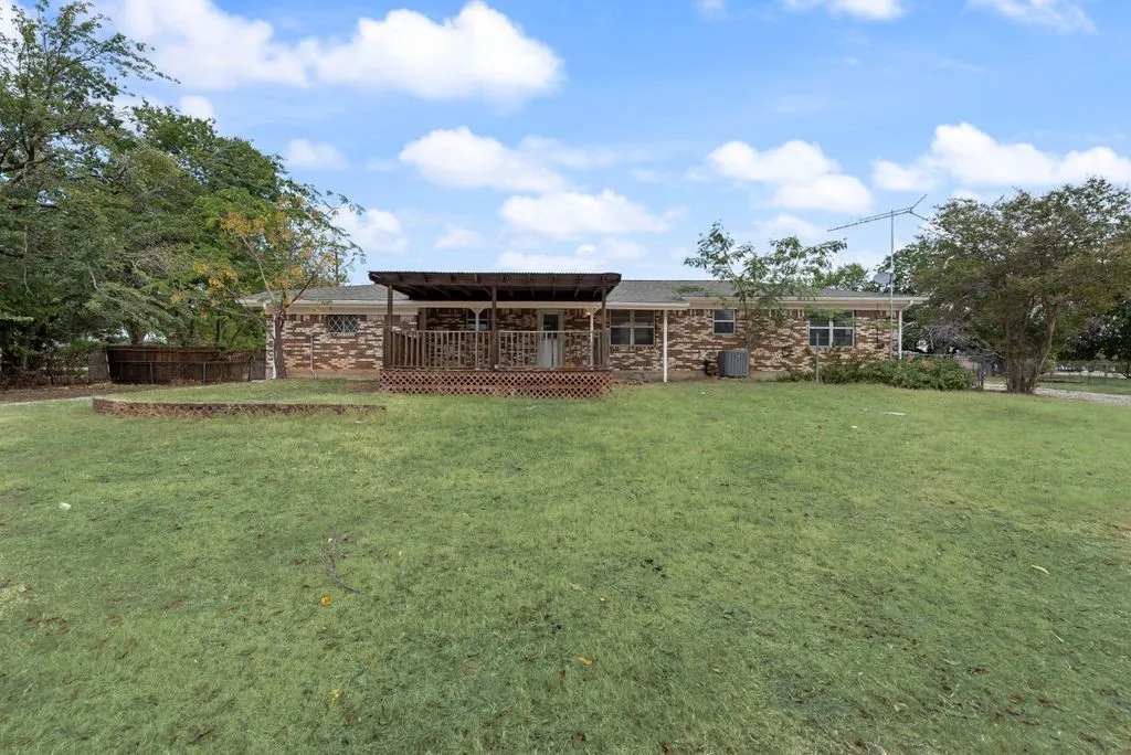 Brick exterior residence featuring a covered wood deck, expansive lawn, and mature trees