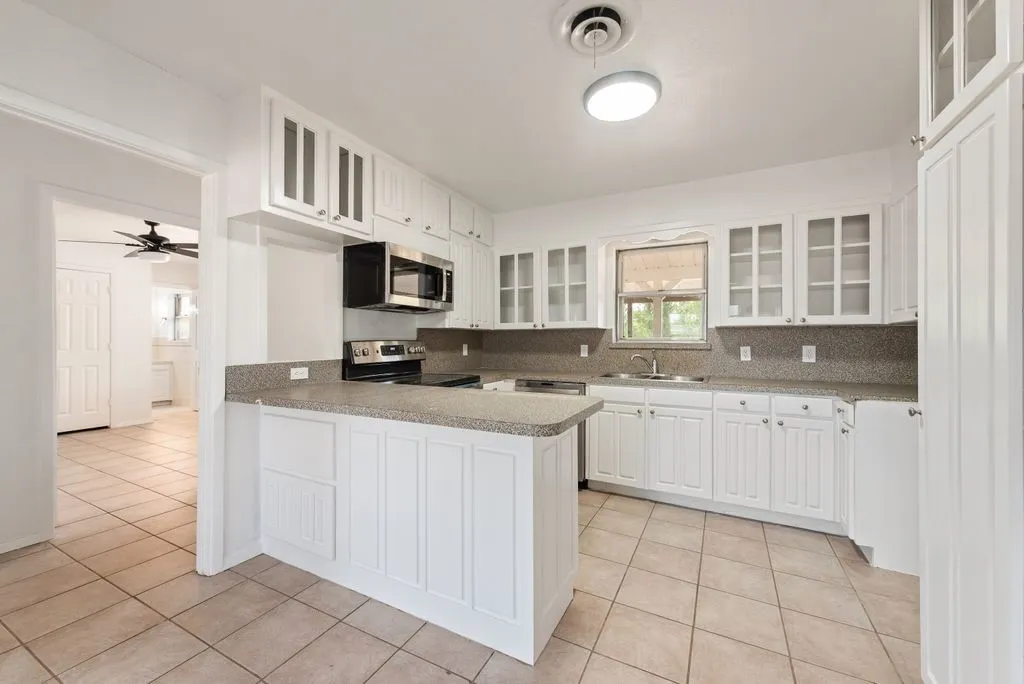 Kitchen featuring white cabinetry, a built-in microwave, tiled flooring, a stainless steel sink, and light-colored countertops
