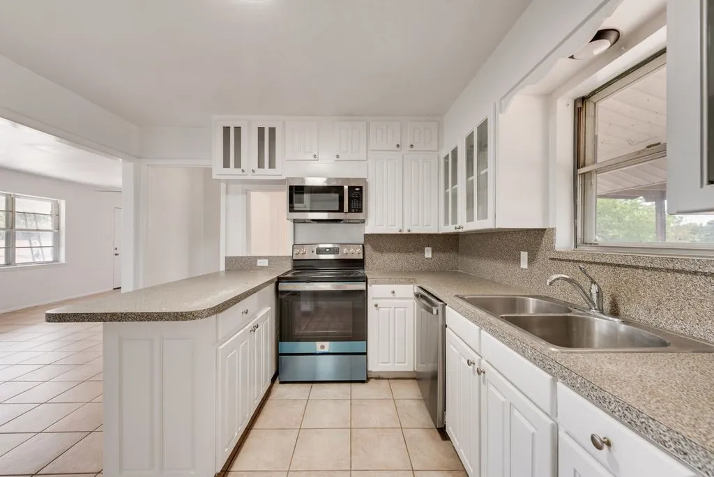 Kitchen featuring white cabinetry, speckled countertops, stainless steel sink, and tile flooring