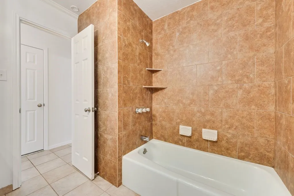 Tub and shower combination with full-height tiled surround, integrated corner shelving, and ceramic floor tiling