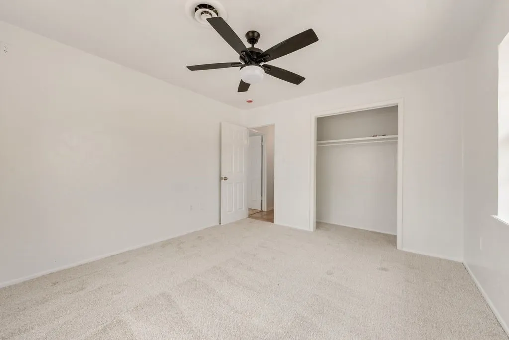 Neutral tone wall finishes, carpeting, ceiling fan with integrated lighting, and an open closet with a hanging rod
