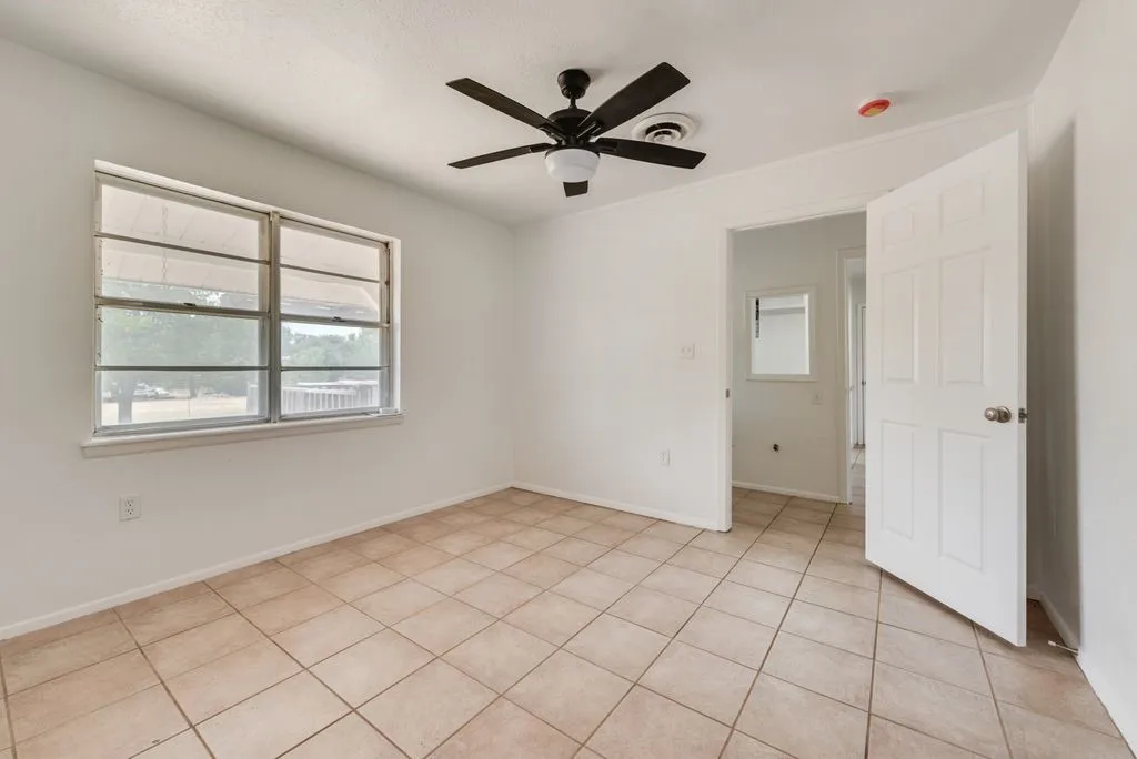 White painted walls, tile flooring, window with exterior scenery, ceiling fan with integrated lighting, and a paneled interior door