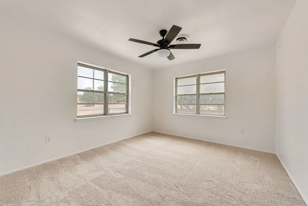 Neutral tone wall finishes, two large windows, installed ceiling fan with integrated lighting, and carpeted flooring