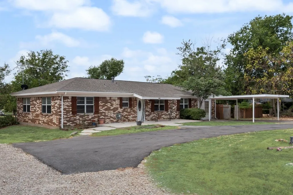 Brick exterior, covered entry, attached carport, paved driveway, and mature landscaping