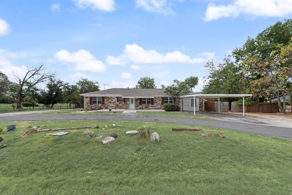 Brick exterior with white trim, a covered carport, and an expansive paved driveway