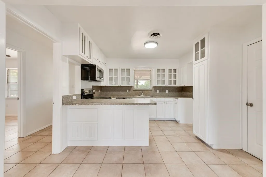 Kitchen with white cabinetry, a black microwave, a black range, stone-finish countertops, and tile​​‌​​​​‌​​‌‌​‌‌​​​‌‌​‌​‌​‌​​​‌​​ flooring