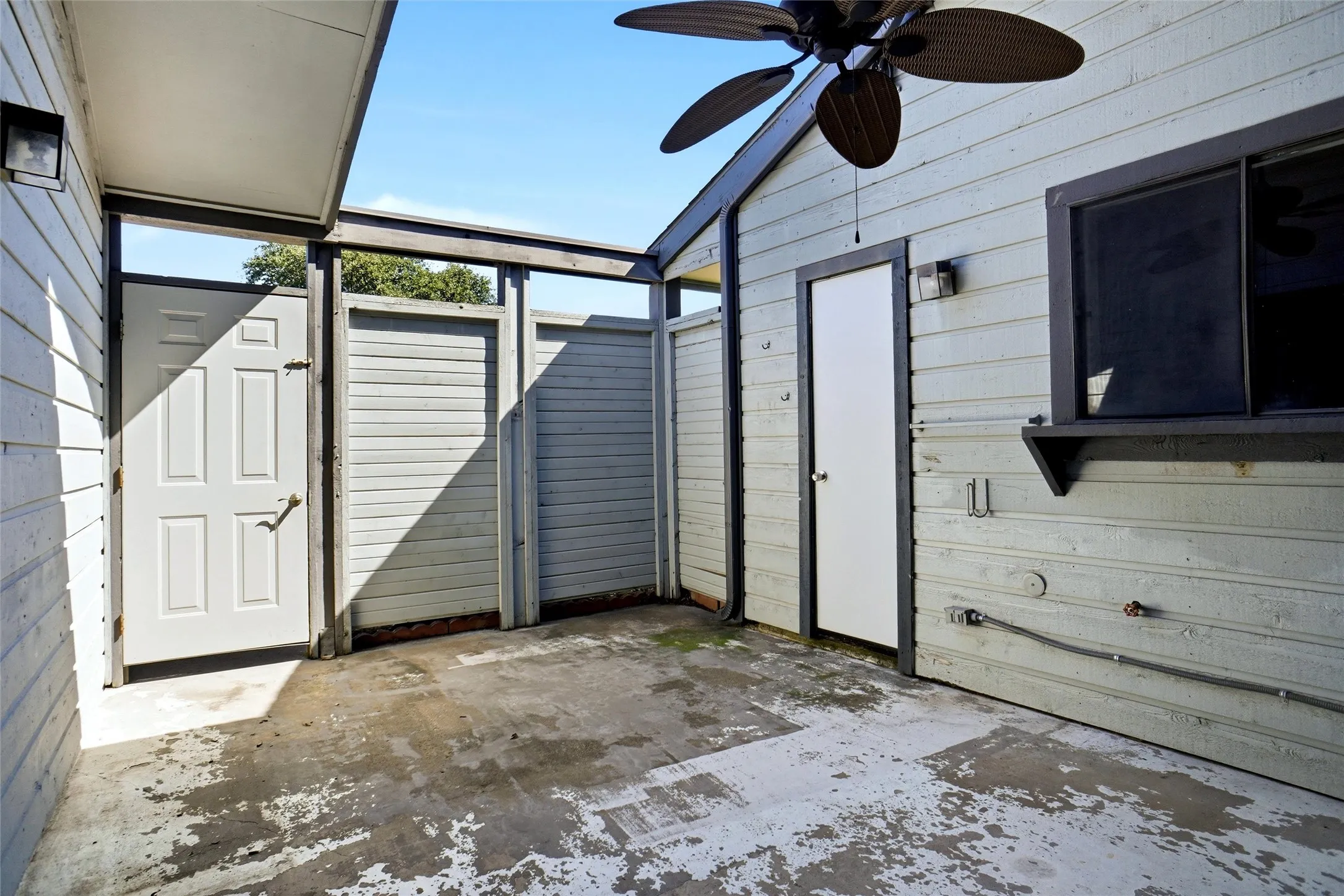 Private outdoor concrete patio entrance with slatted wood fencing, exterior lighting, storage closet and an overhead ceiling fan