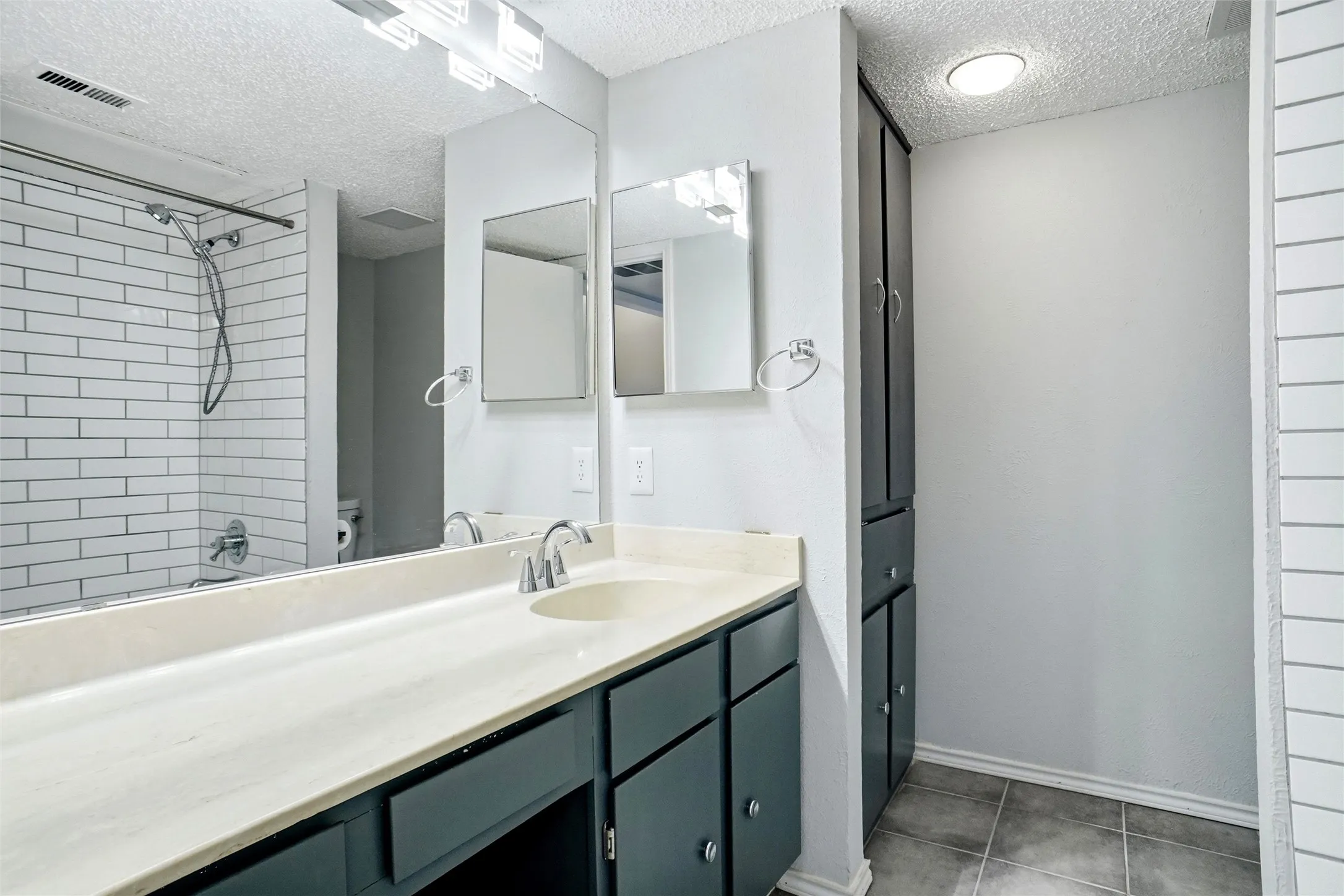 Vanity with integrated sink, Subway tile shower surround, Mirrored medicine cabinet, Overhead vanity lighting, and Linen closet