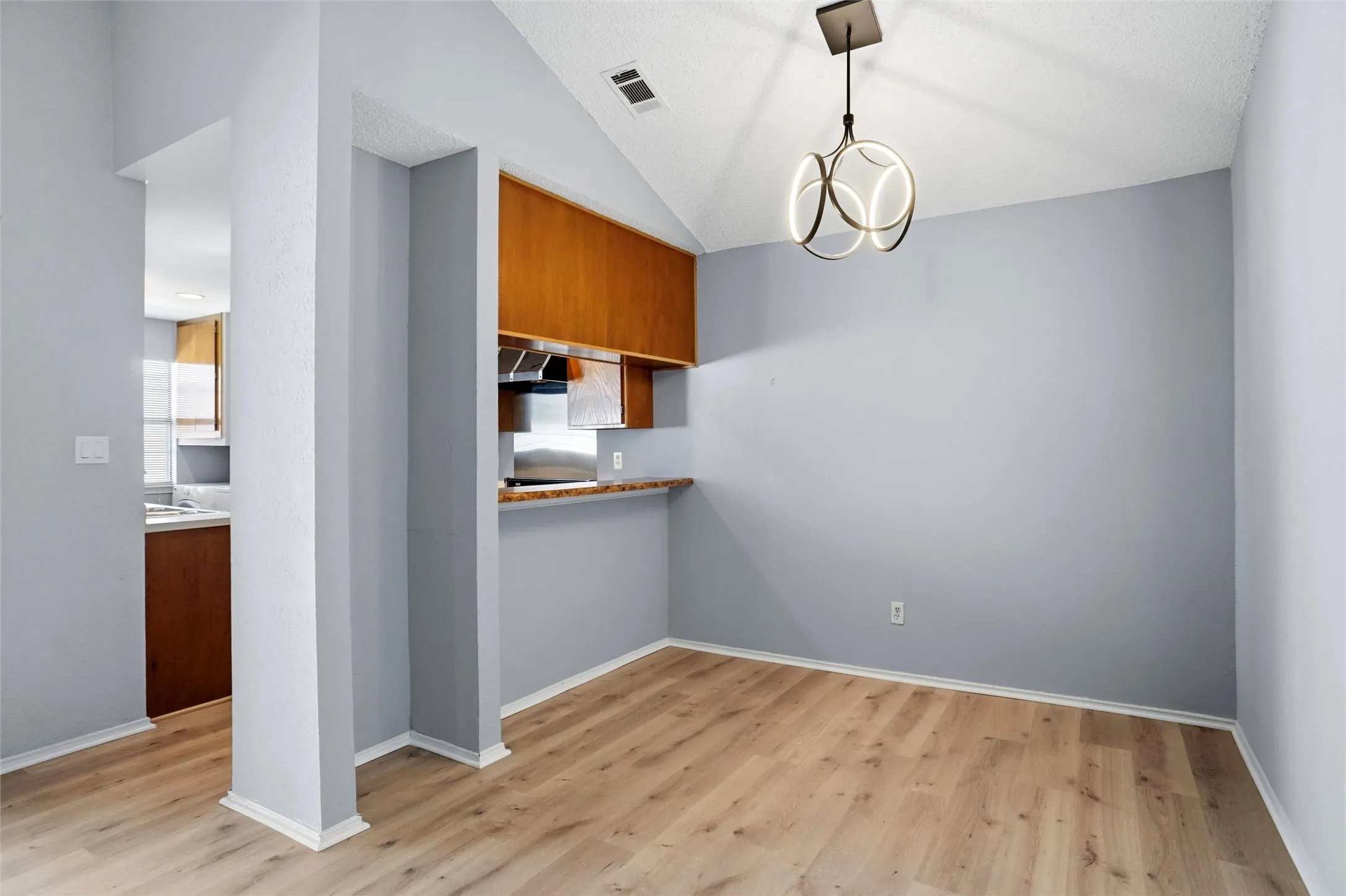 Vaulted ceiling featuring a contemporary chandelier, LVP flooring, half wall with pass-thru bar, warm-toned wood cabinetry