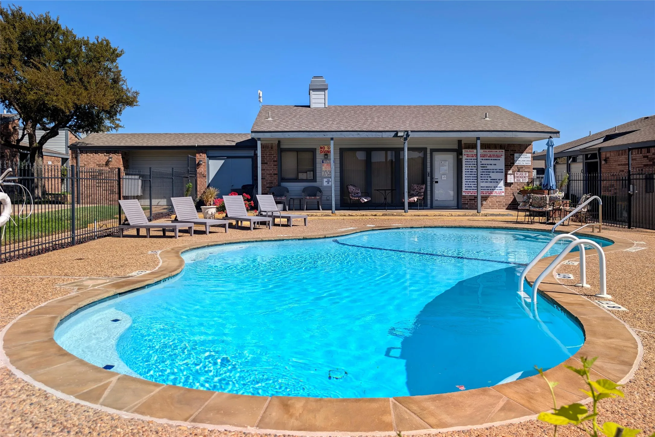 Resort-style pool area featuring a freeform swimming pool with integrated steps, surrounding exposed aggregate concrete decking, and access to Community Clubhouse