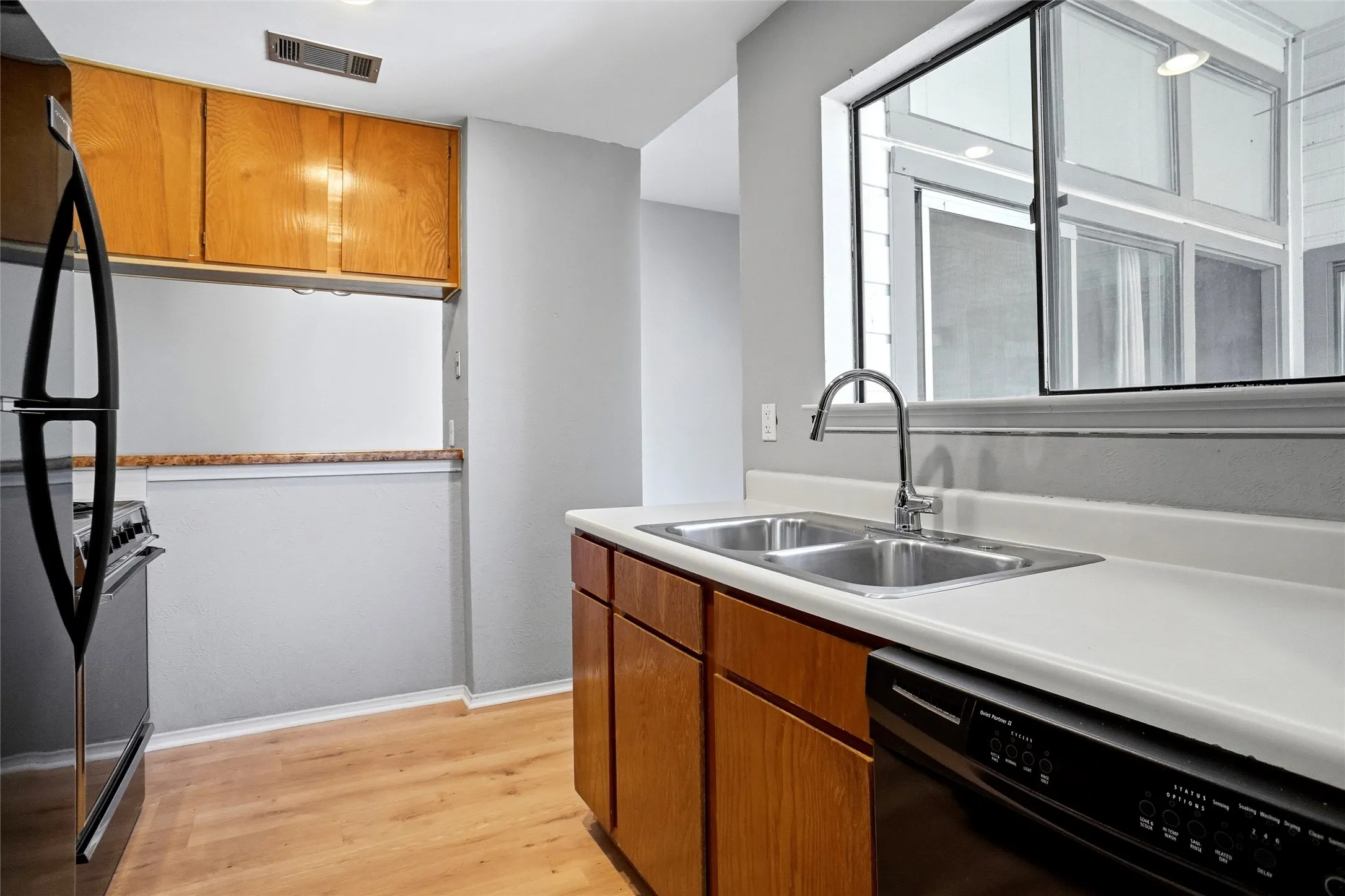 Kitchen featuring LVP flooring, wood cabinetry, dual stainless steel sink, and a black appliances