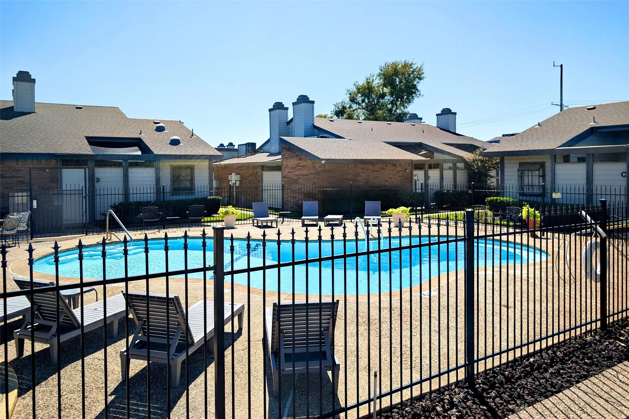 Fenced swimming pool with abundant decking and furniture.