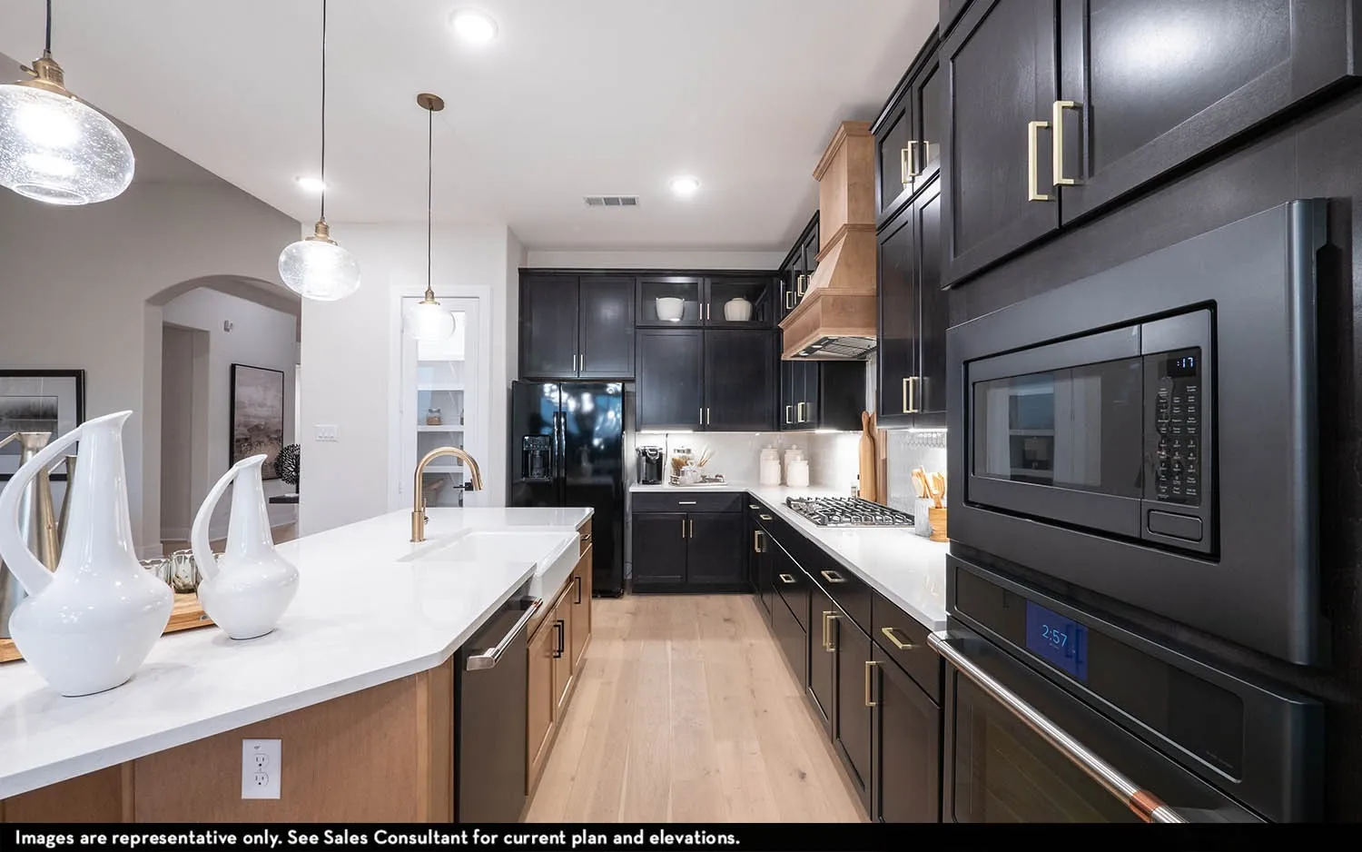 Kitchen featuring dark wood cabinetry with gold-tone hardware, white countertops, built-in black appliances, a wood-finish range hood, and a kitchen island with a farmhouse sink