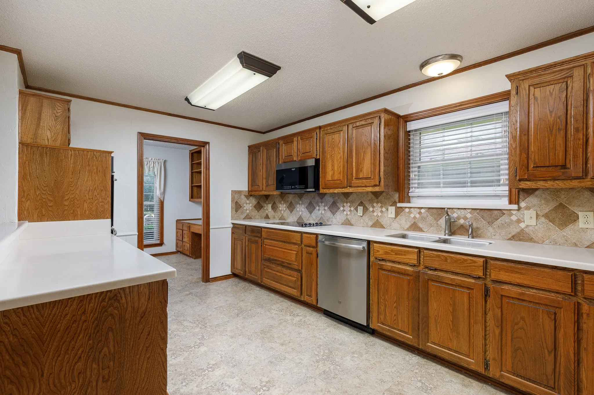 Wood cabinetry and white countertops define this kitchen space, featuring a stainless steel dishwasher, a built-in microwave, and a decorative tile backsplash