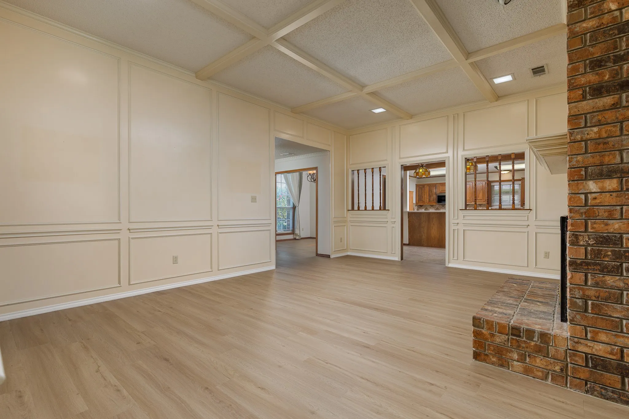 Wood-finish flooring, brick-clad fireplace with hearth, coffered ceiling, and wainscoting paneling