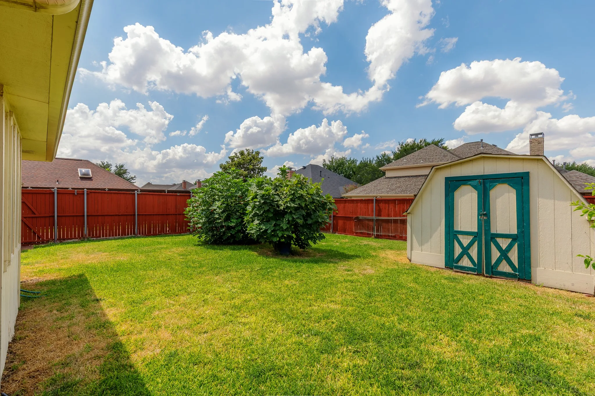 Expansive backyard featuring a manicured lawn, established shrubbery, full perimeter fencing, and a detached storage shed