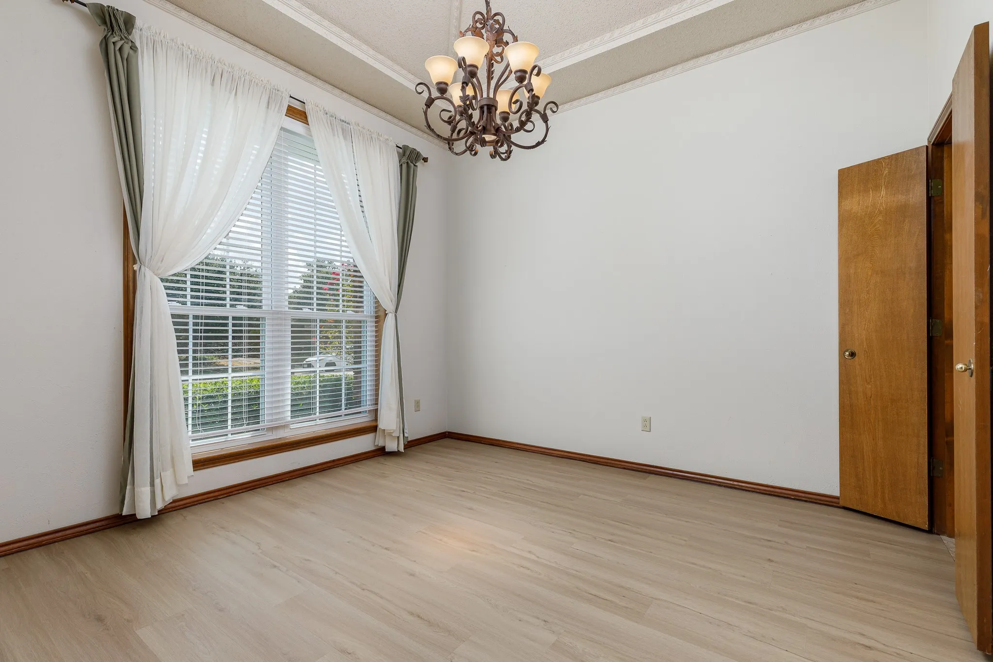 Spacious room featuring light wood-finish flooring, a large window, and an ornate chandelier