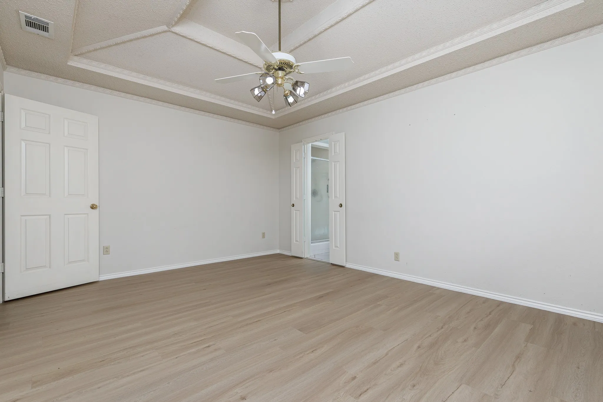 Recessed ceiling with decorative trim, wood-finish flooring, ceiling fan with integrated lighting, and panel doors