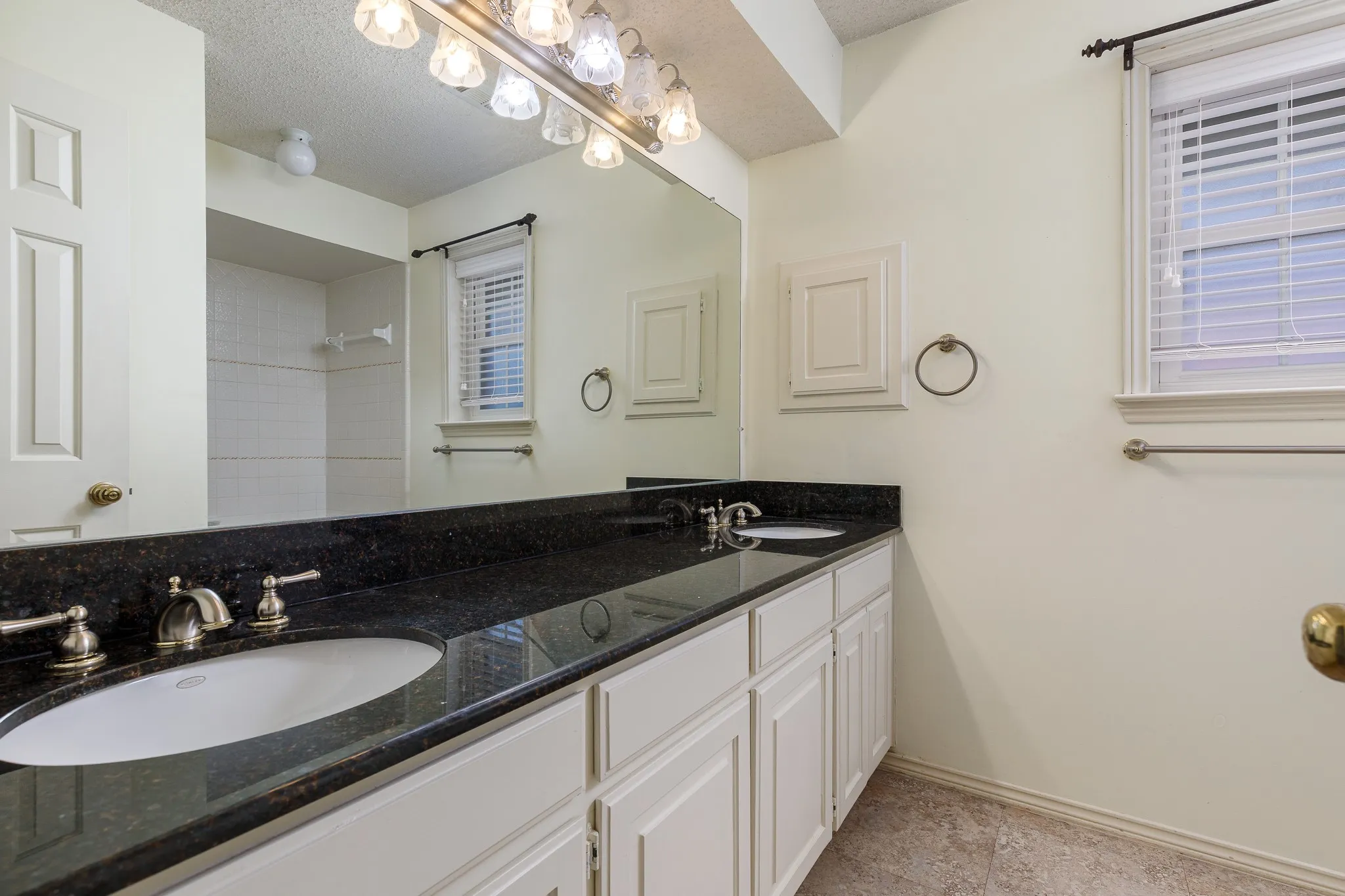 Dual vanity with dark granite-style countertop, white cabinetry, and brushed nickel fixtures