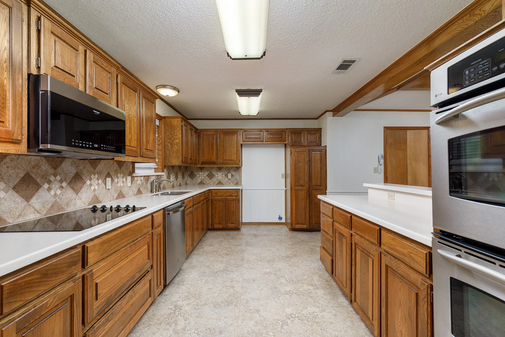 Expansive kitchen featuring wood cabinetry, white countertops, stainless steel appliances, and a tiled backsplash