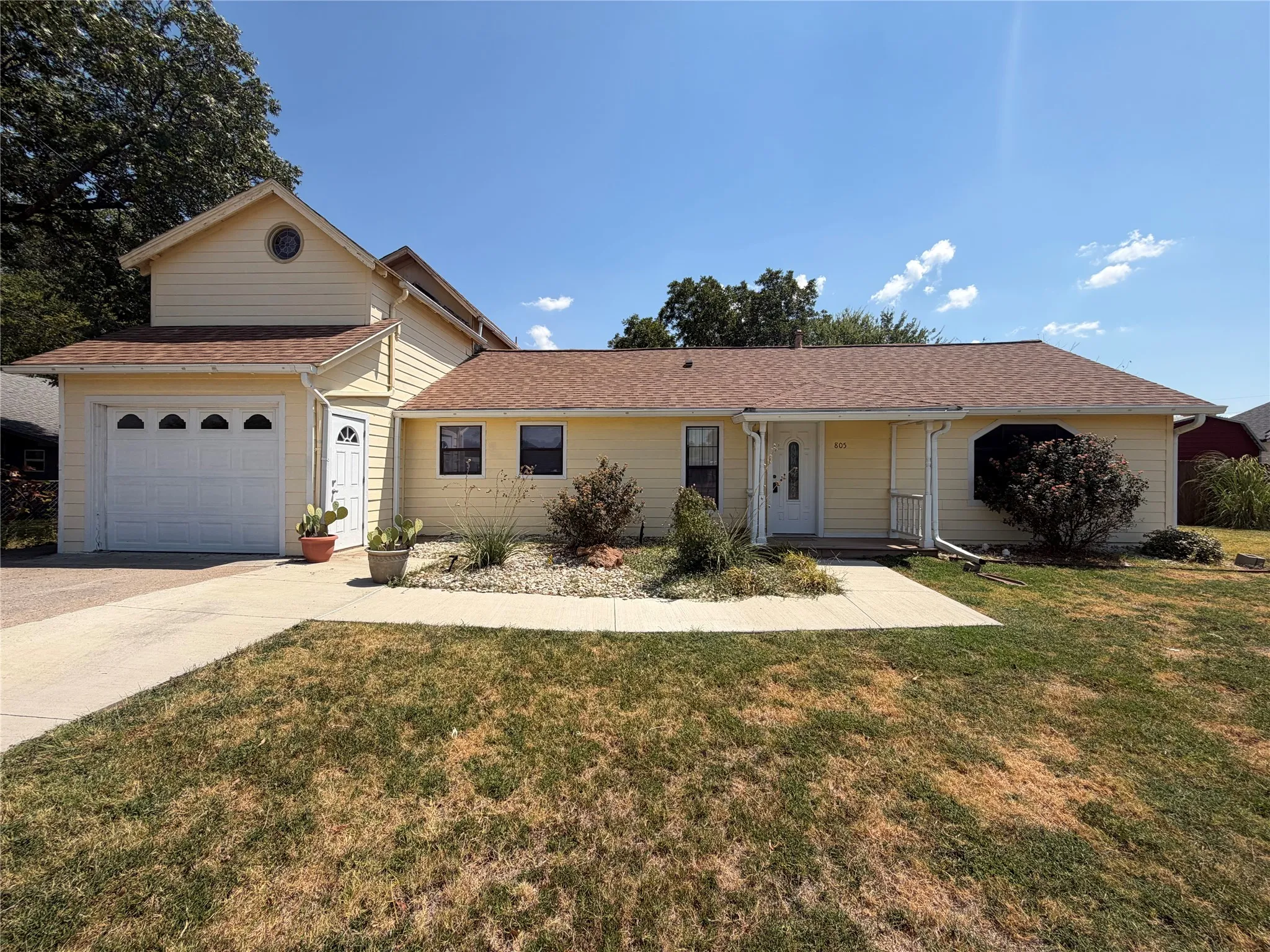 Yellow siding exterior with a brown shingle roof, attached garage with white door, front entry porch, and a bay window